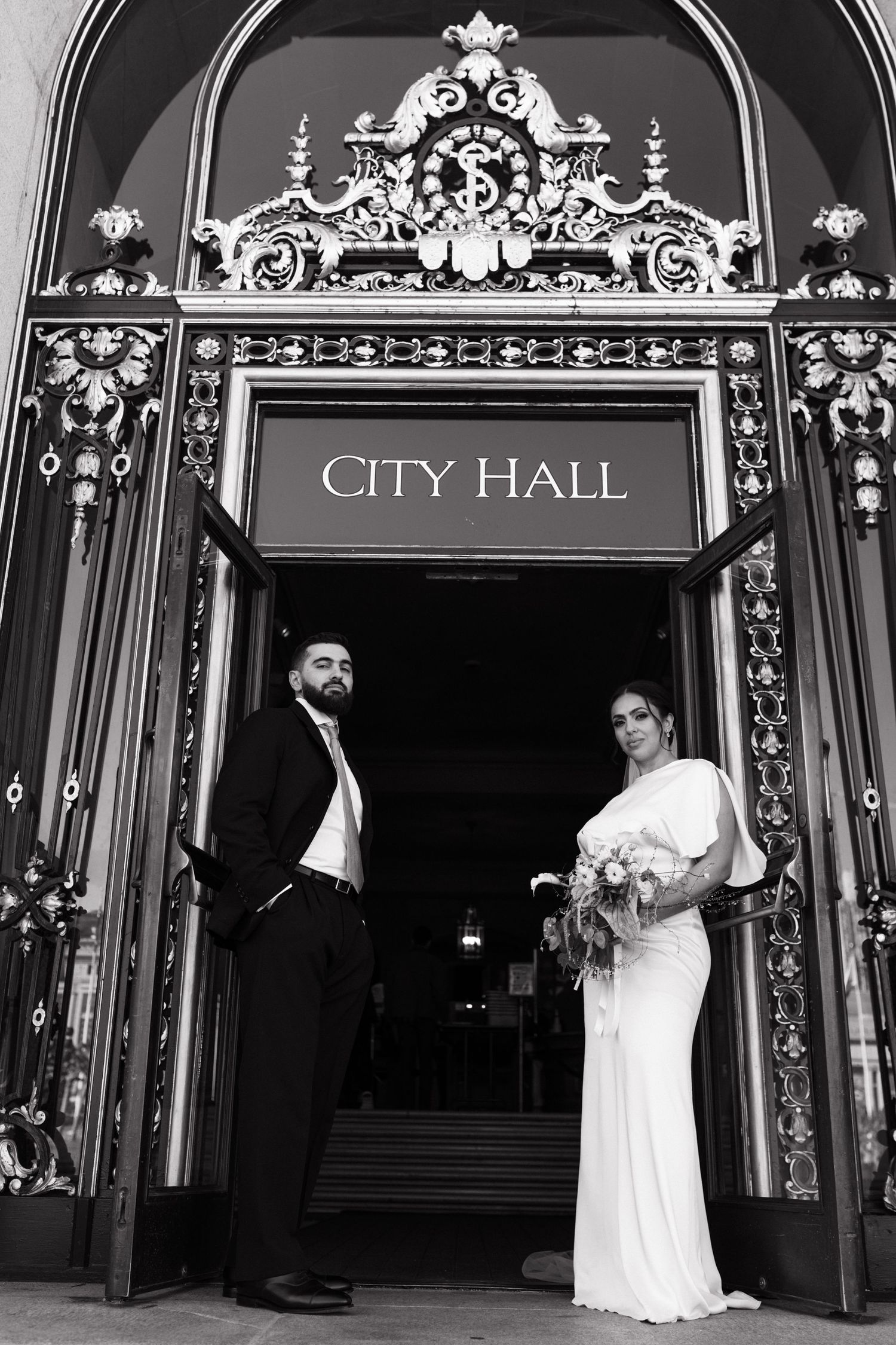 Couple with bouquet at the City Hall entrance at a San Francisco elopement, by Sammy Aucella Photography