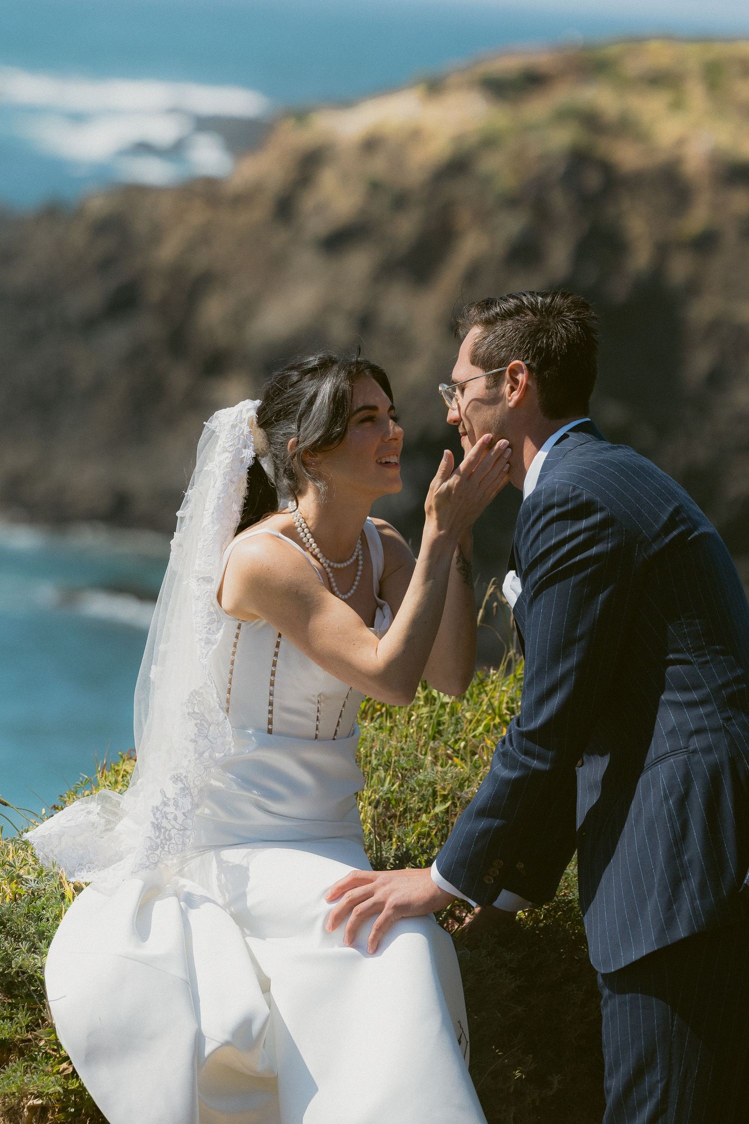 Groom touching the bride's face by the ocean during a Mendocino cliffs first look, by Sammy Aucella Photography
