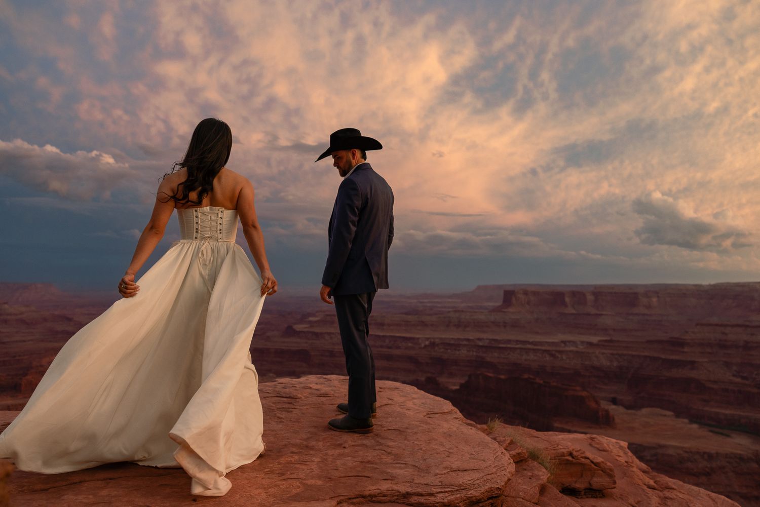 Cowboy groom and bride at a Moab cliff edge in Utah, by Sammy Aucella Photography