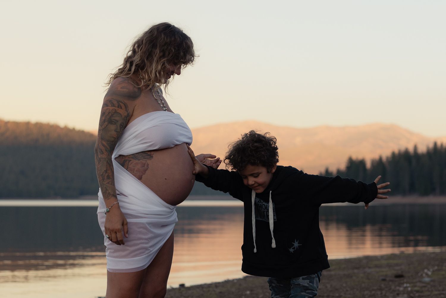 Expecting couple by a calm lake at sunset, tender maternity session