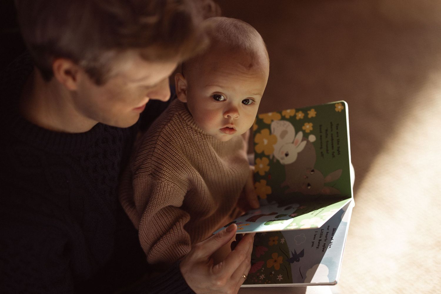 Parent reading a picture book to their baby in soft window light, tender lifestyle newborn and family session