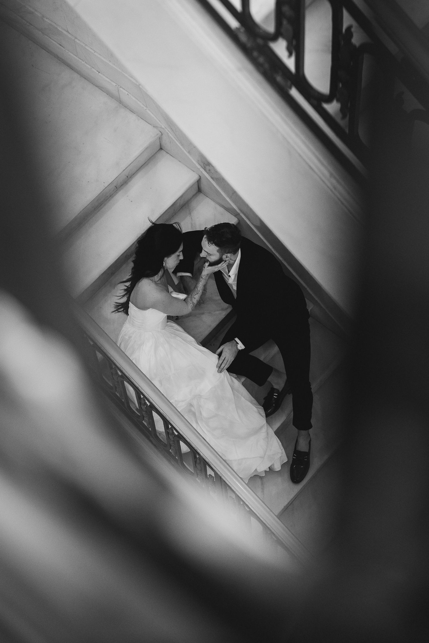 Black-and-white photo of a couple embracing viewed through a circular architectural frame, artistic wedding portrait