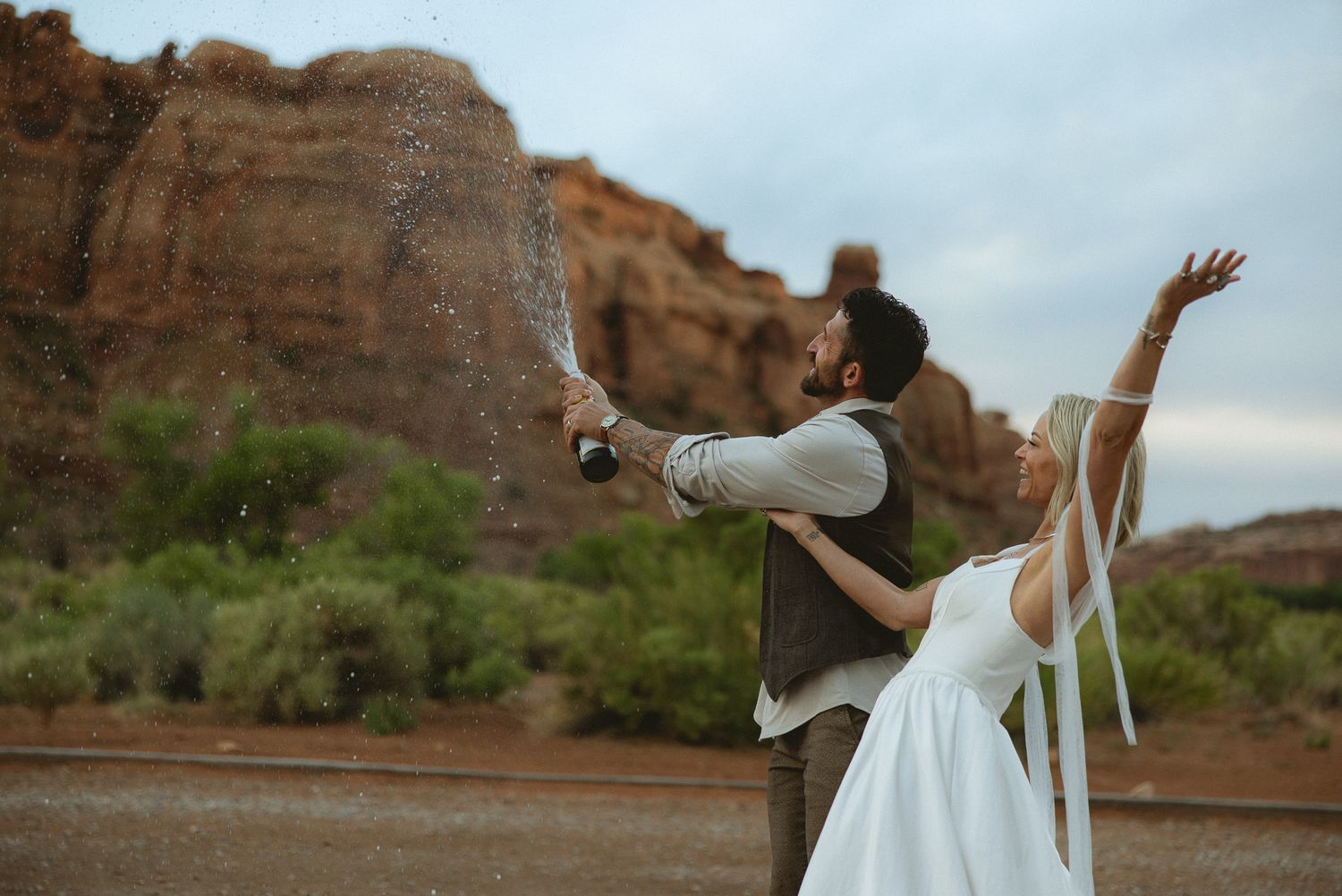 Groom spraying champagne at a Moab rock formation in Utah, by Sammy Aucella Photography