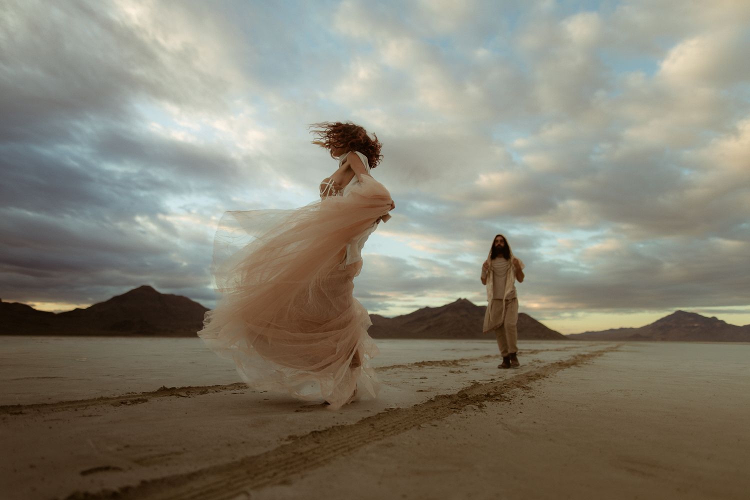 Bride twirling her gown on the Bonneville Salt Flats with mountains beyond, by Sammy Aucella Photography