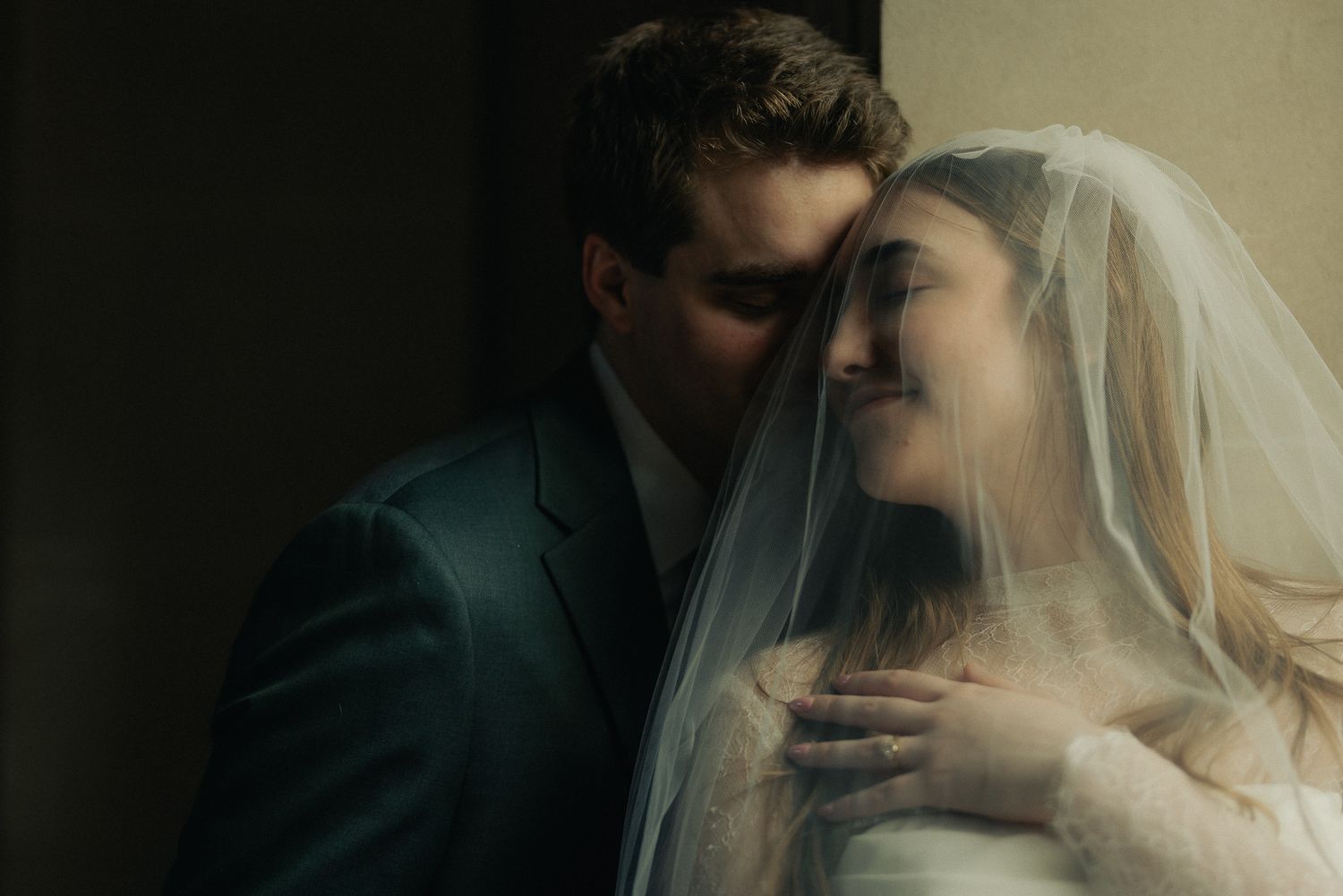 Groom embracing his veiled bride in warm, moody light, intimate and romantic wedding portrait