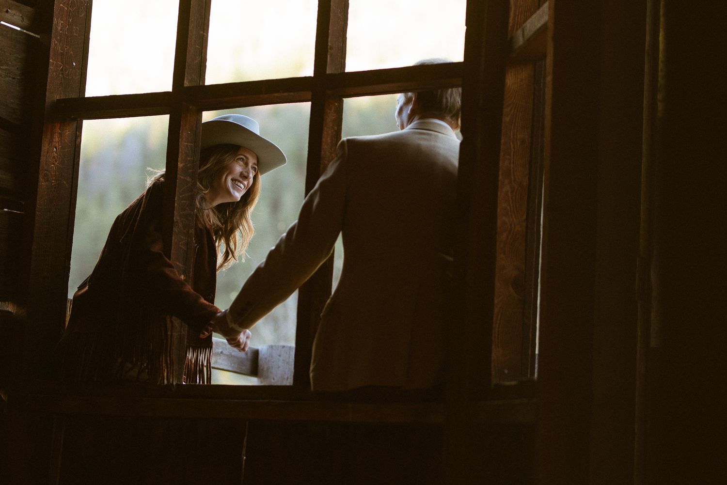 Couple embracing framed by a rustic cabin window, intimate Western elopement photography