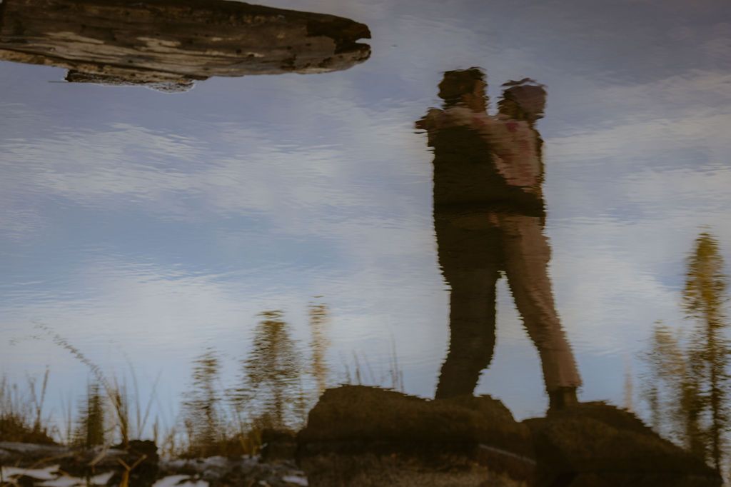 Couple embracing mirrored in still water in a creative reflection at golden hour, artistic elopement photography