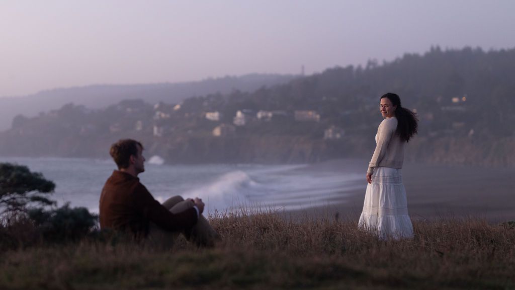 Couple sharing a glance on a coastal bluff at dusk with the bay behind them, romantic Northern California engagement session