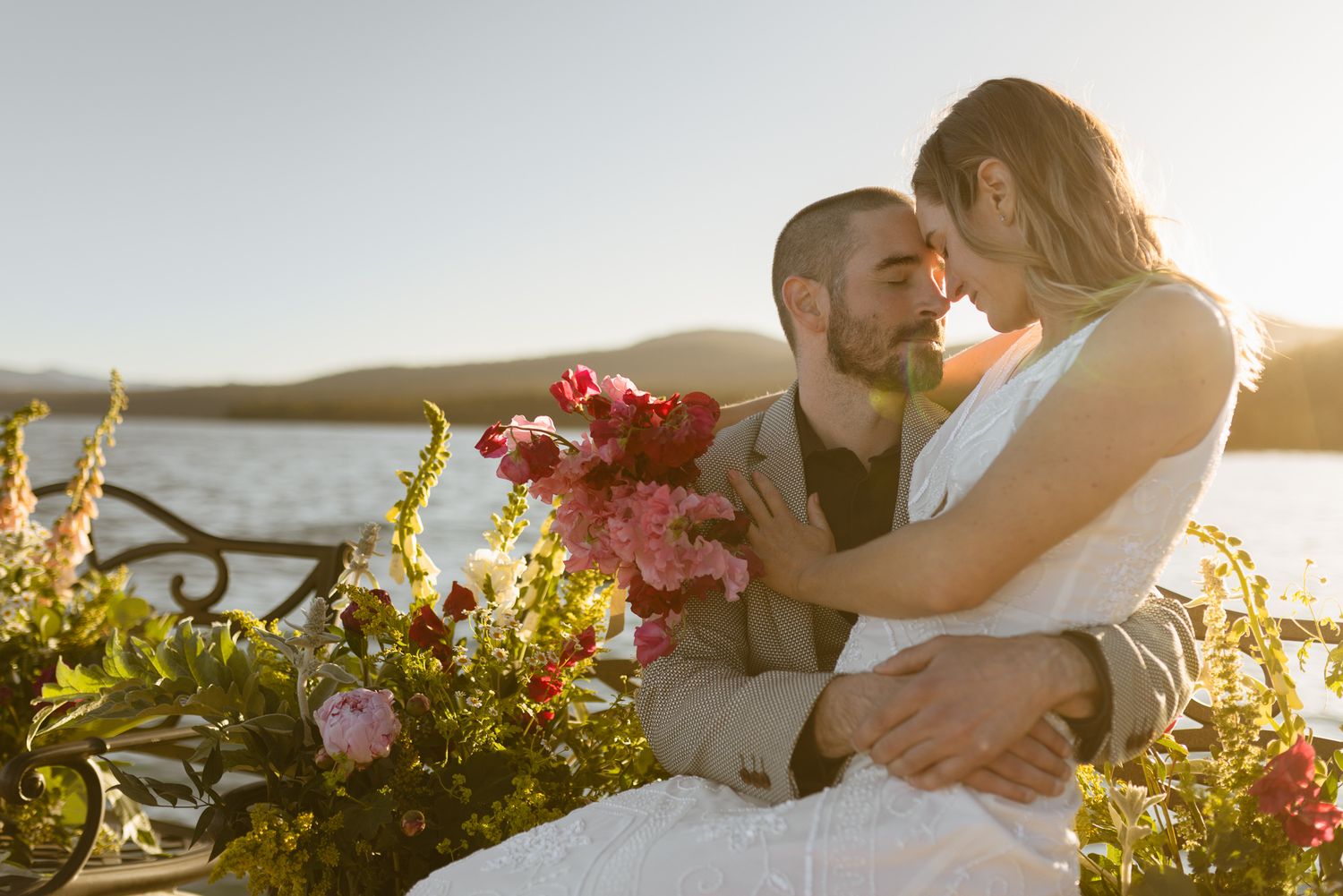 Couple embracing by the lake amid lush florals at a Lake Tahoe wedding at sunset, by Sammy Aucella Photography