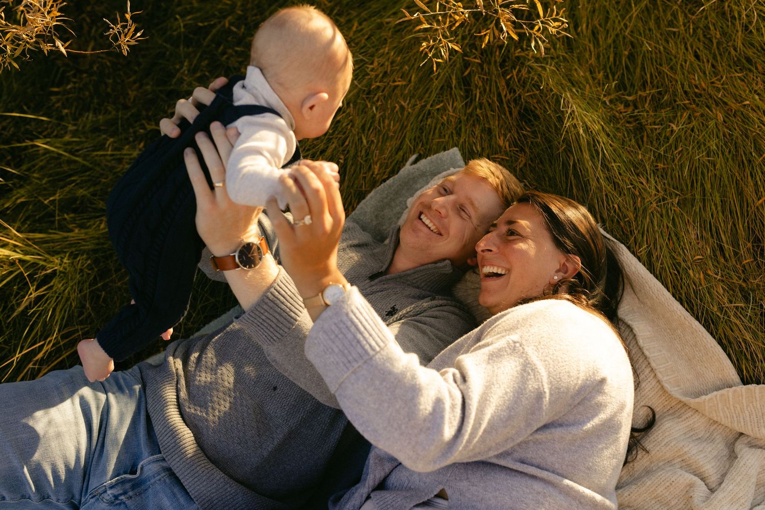 Parents playing with their baby in golden grass at sunset, warm candid family session