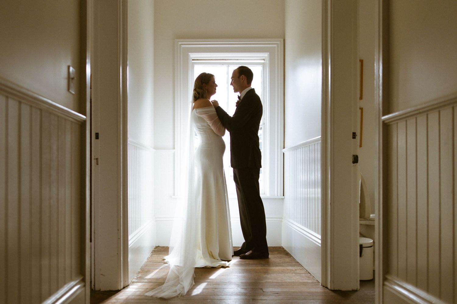 Couple silhouetted embracing in a sunlit doorway at the end of a hallway, intimate backlit elopement portrait