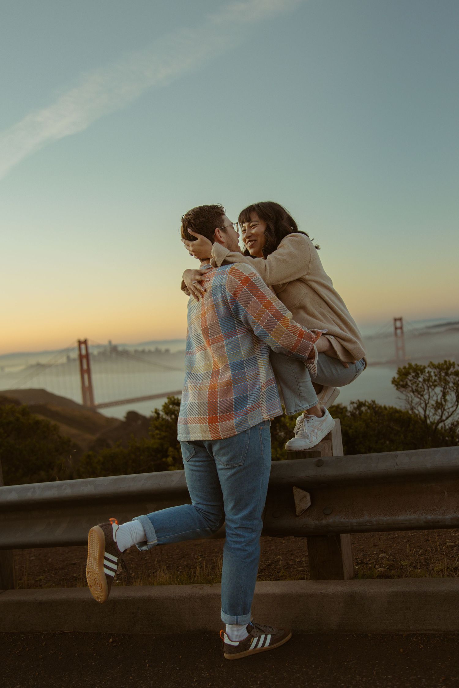 Couple embracing with the Golden Gate Bridge above the fog behind them, romantic San Francisco engagement session