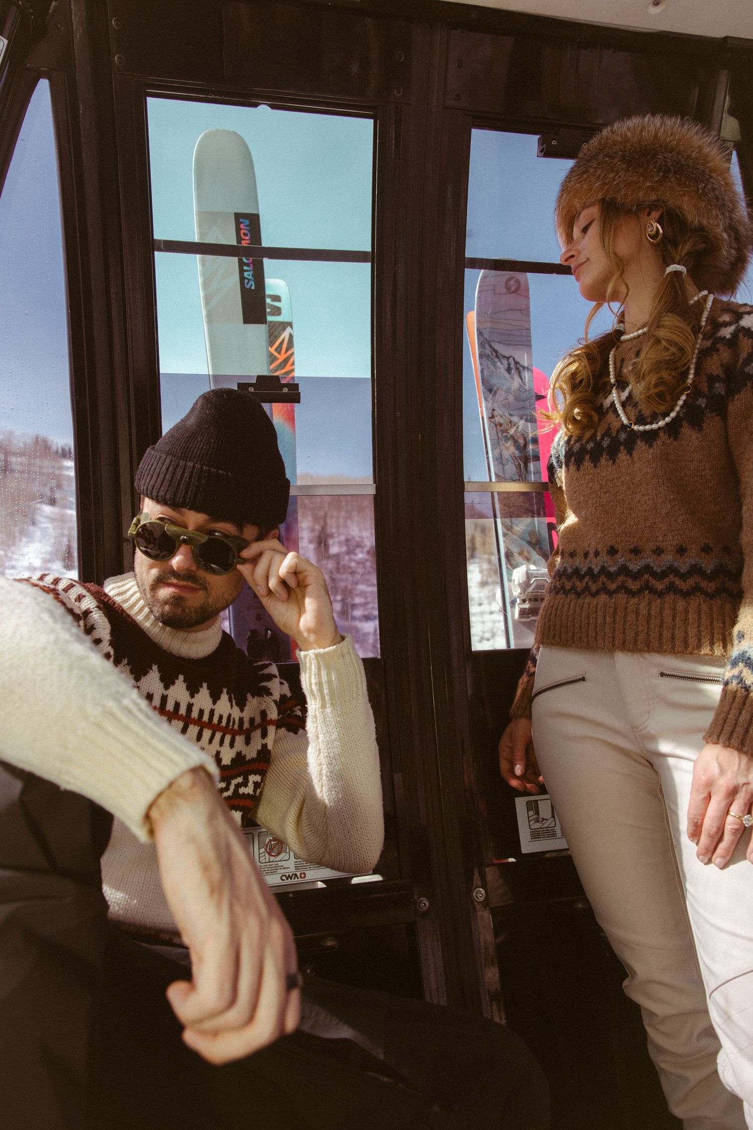 Stylish couple in vintage ski wear inside Aspen ski gondola during creative engagement photo session by Sammy Aucella Photography