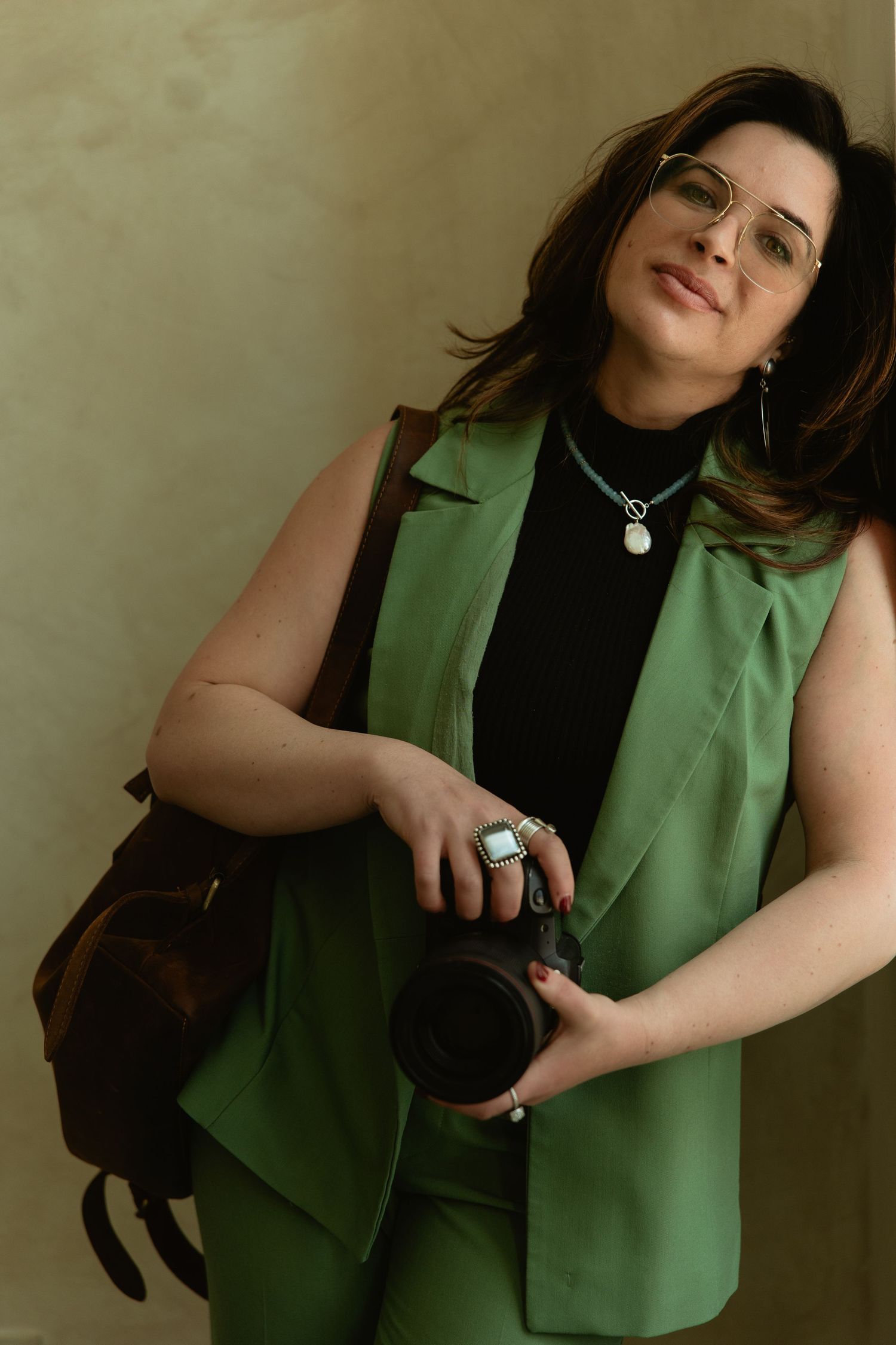 Photographer in a green suit holding her camera in soft window light, confident personal branding portrait for creatives
