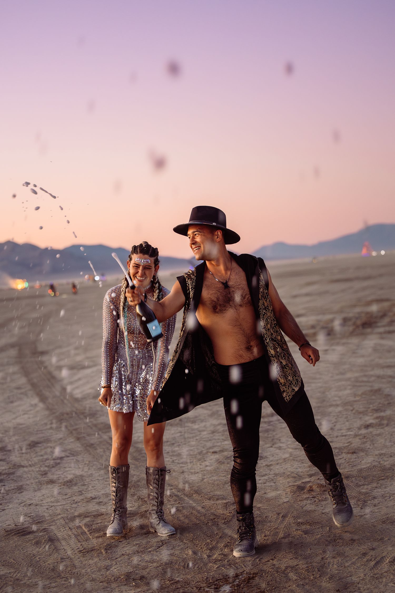 Couple on the playa as hot air balloons drift at sunset, whimsical desert festival photography