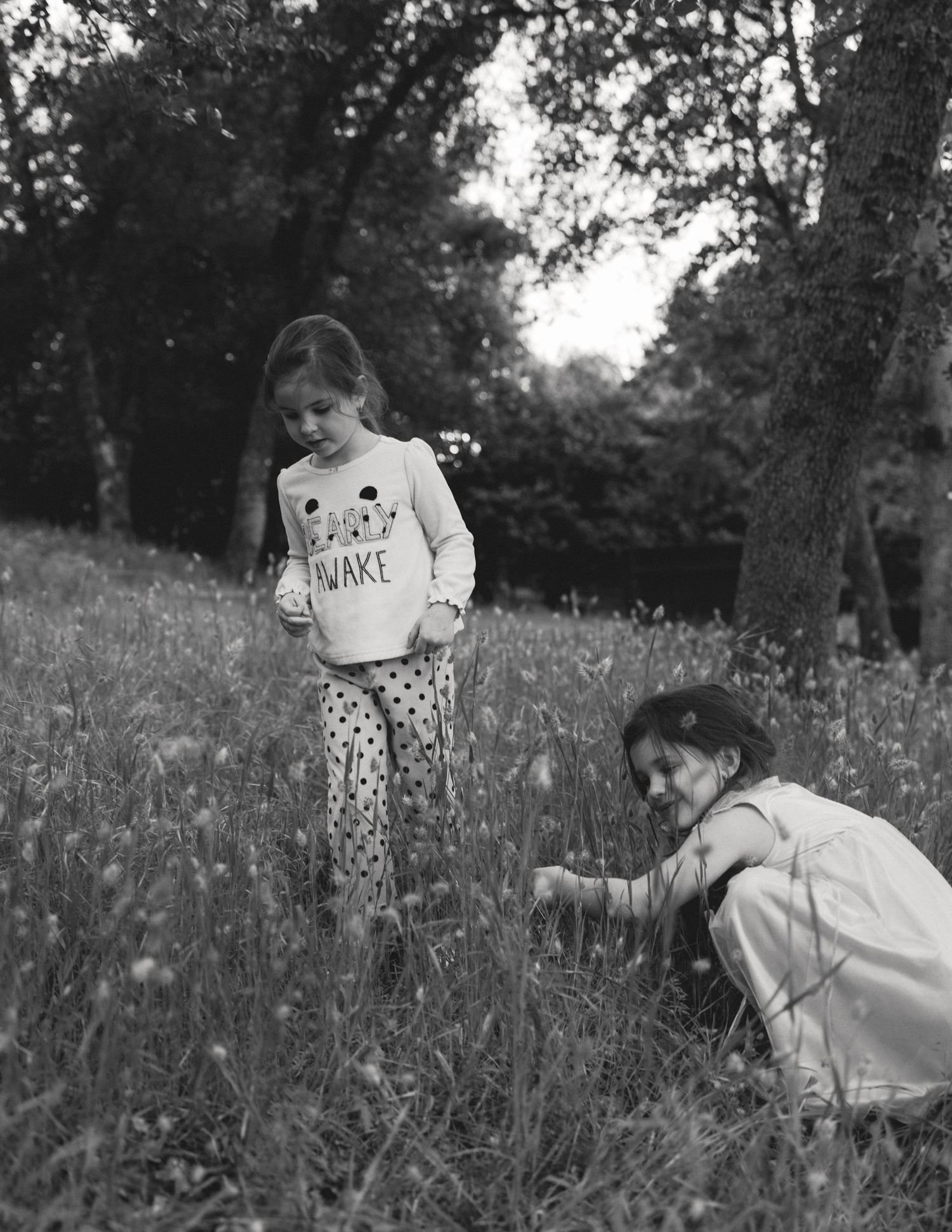 Black-and-white photo of a parent crouching beside their child in a wildflower meadow, candid lifestyle family session