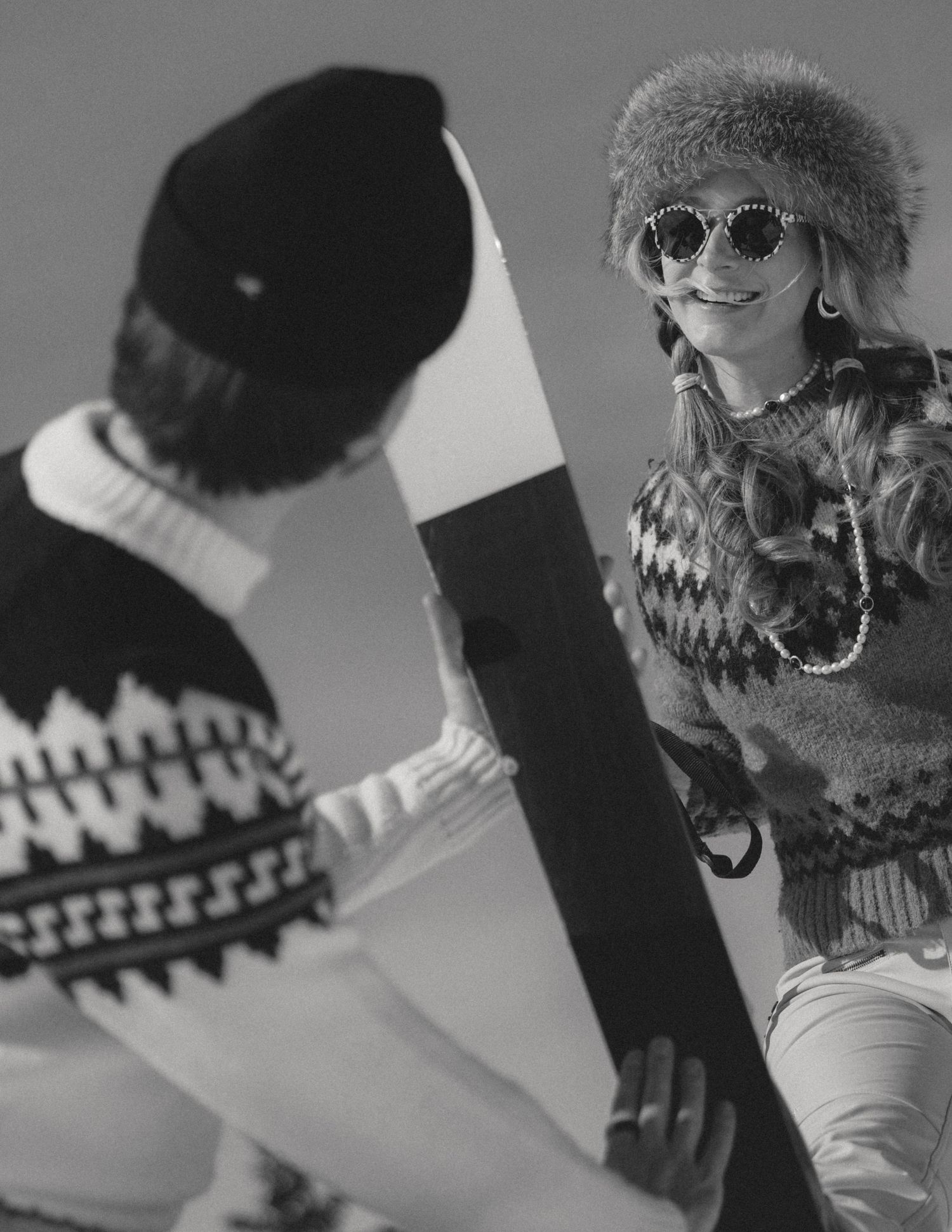 Black-and-white photo of a playful couple in hats and sunglasses laughing together, fun candid engagement session