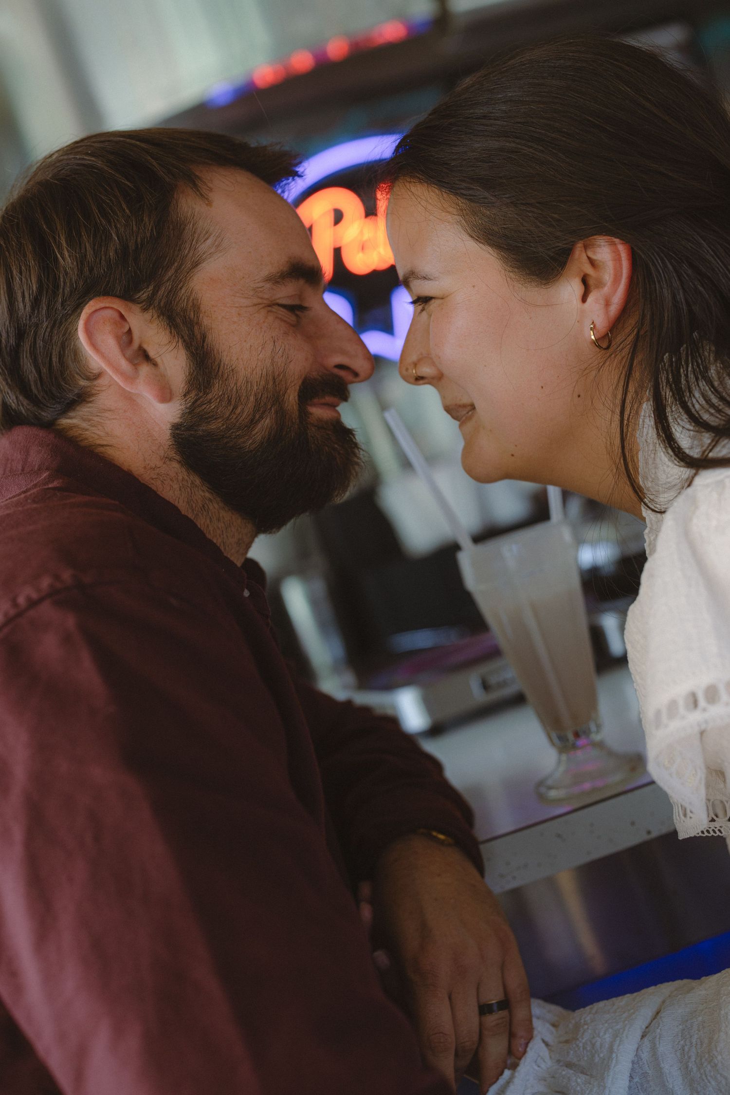 Couple resting forehead to forehead in an intimate moment at a neon-lit bar, romantic date-night engagement session