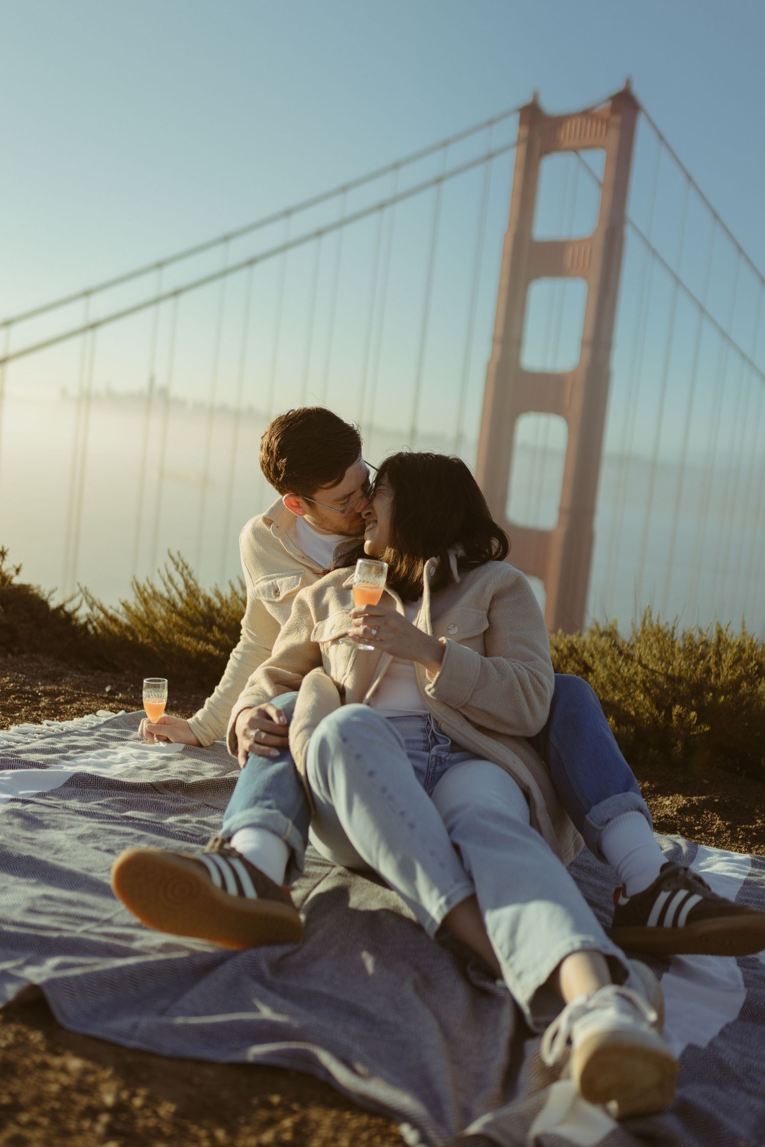 Couple sharing a picnic on a blanket with the Golden Gate Bridge rising from the fog behind them, San Francisco engagement session