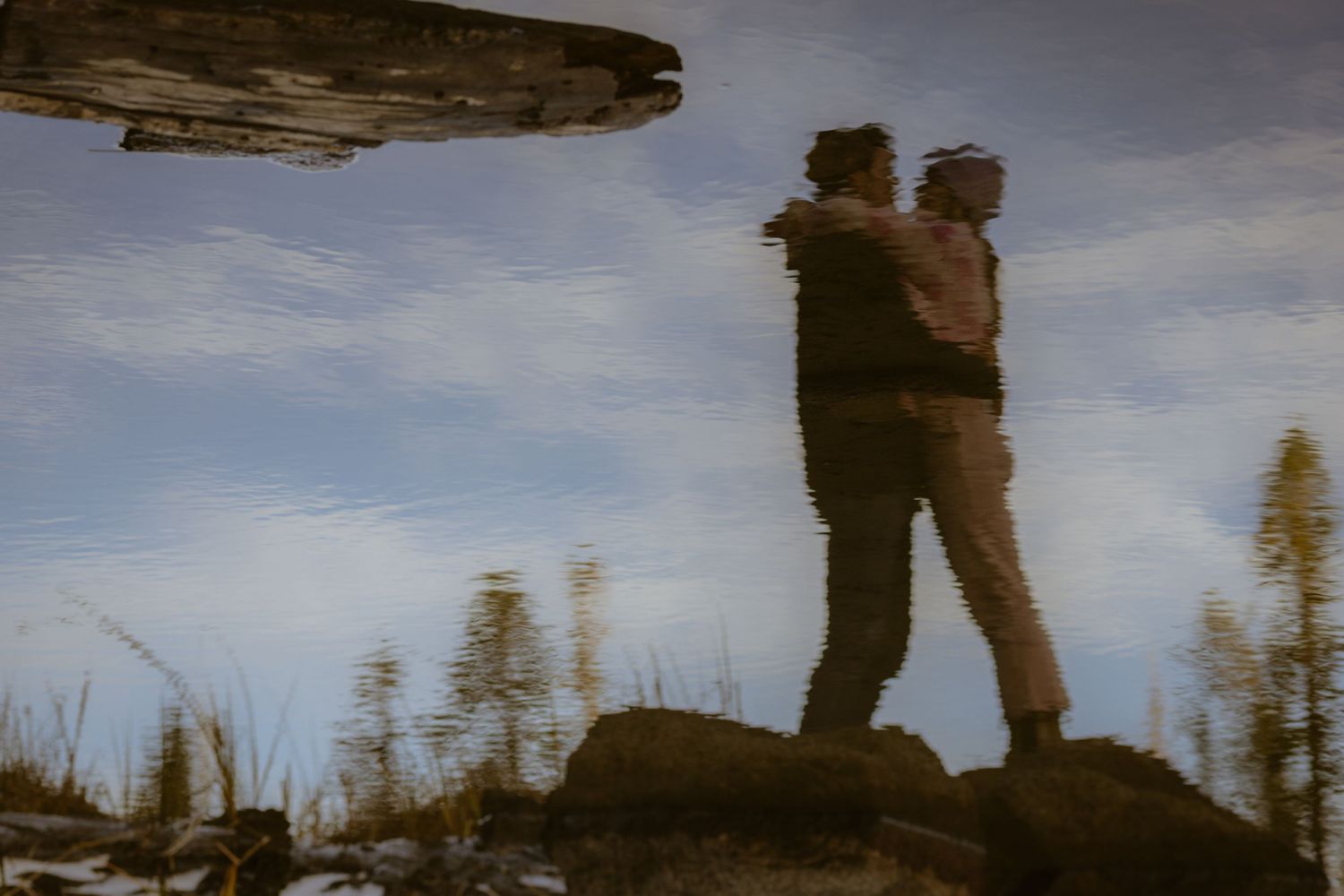 Couple embracing mirrored in still water in a creative reflection at golden hour, artistic elopement photography
