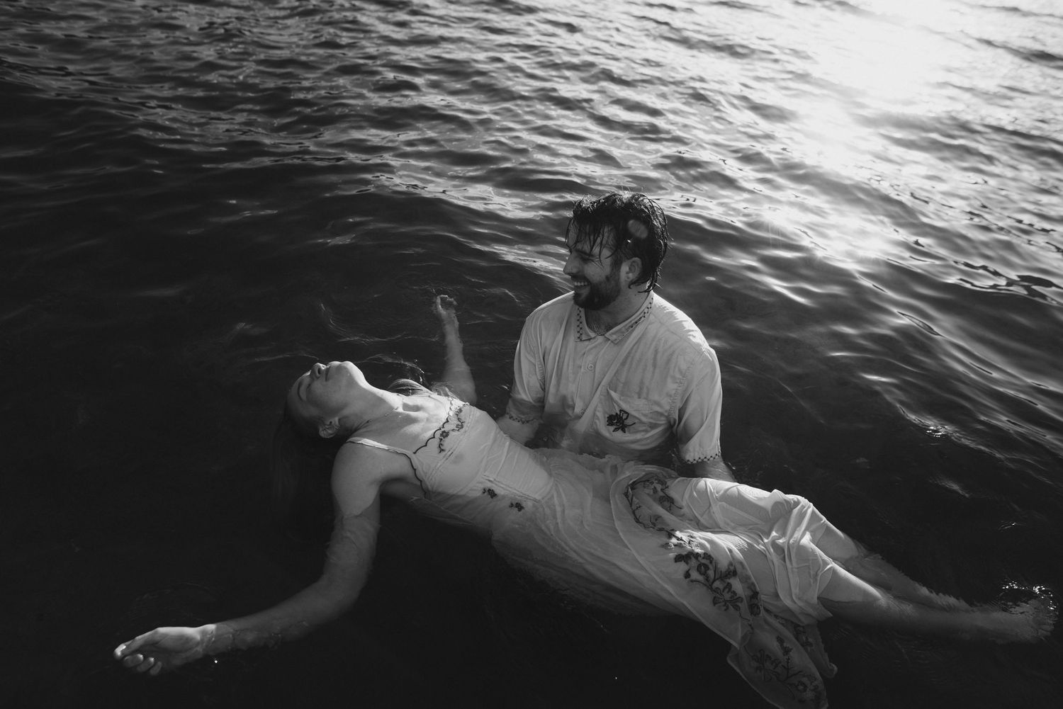 Groom cradling his bride as she floats in a calm alpine lake, romantic black-and-white couples story session