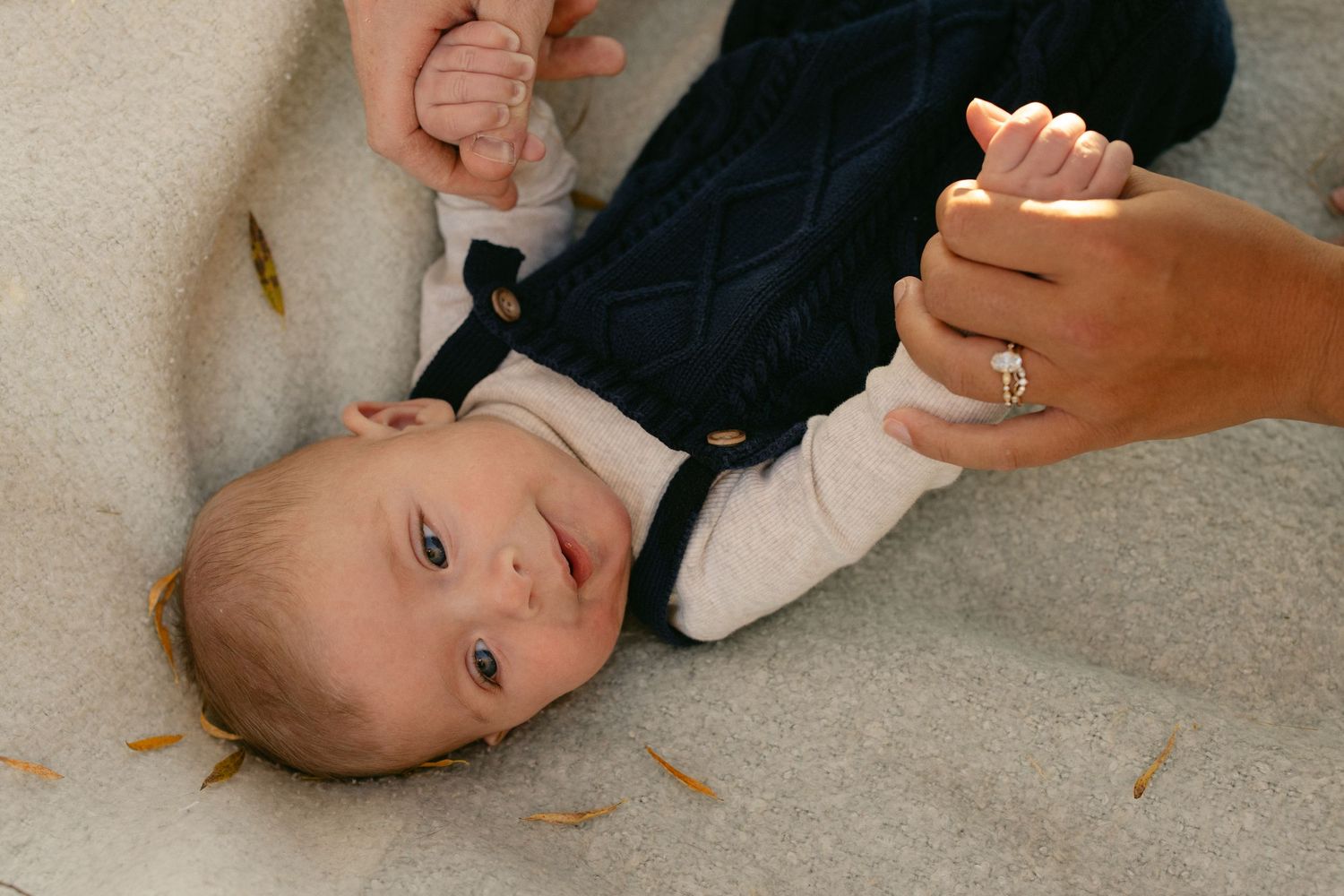 Newborn baby lying on a blanket while a parent holds their tiny feet, tender family newborn photography