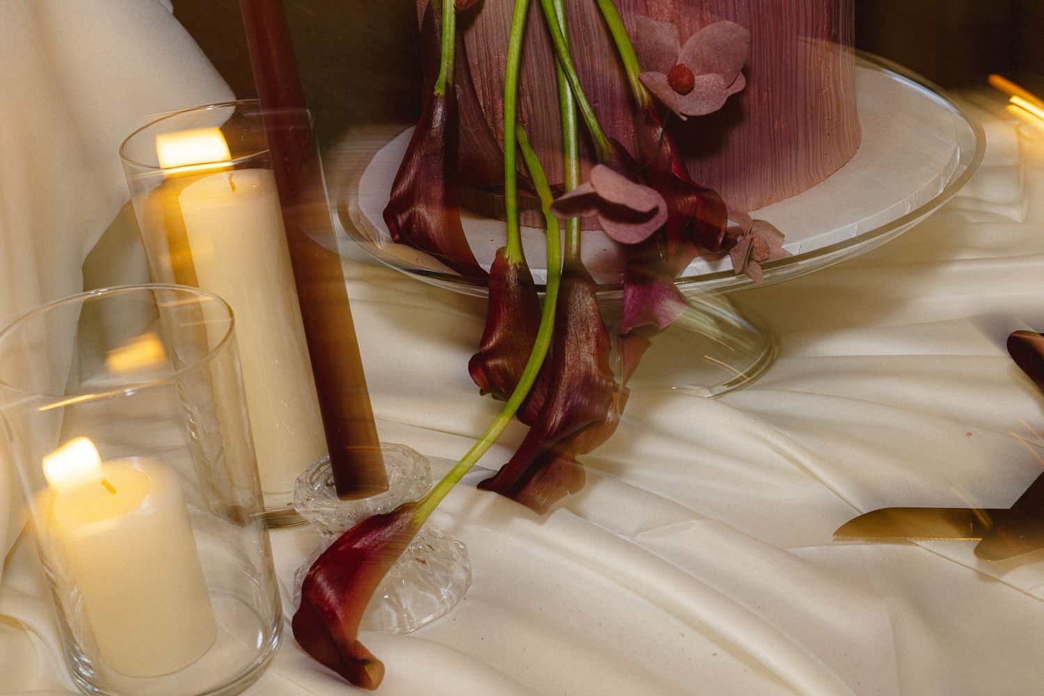 Candlelit wedding reception table detail with calla lilies and pillar candles on white linen, elegant decor close-up