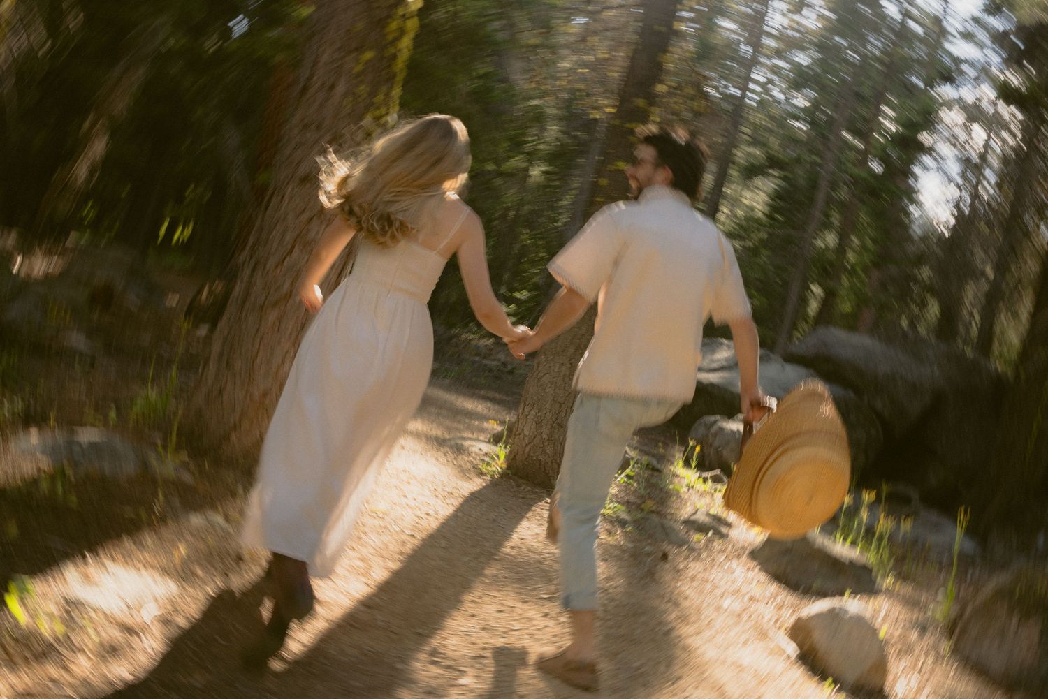 Couple running hand in hand through a sunlit pine forest, motion-blurred and playful destination story session