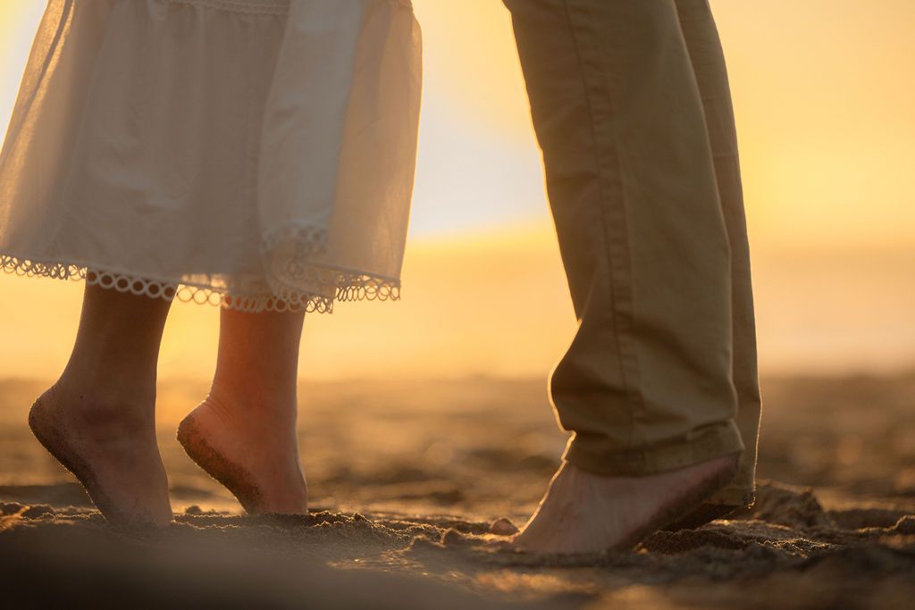 Close-up of a couple's bare feet standing together on the sand at golden hour, tender coastal elopement detail