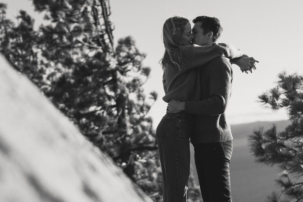 Black and white image of a couple embracing among the pines on a hillside, intimate forest couples session