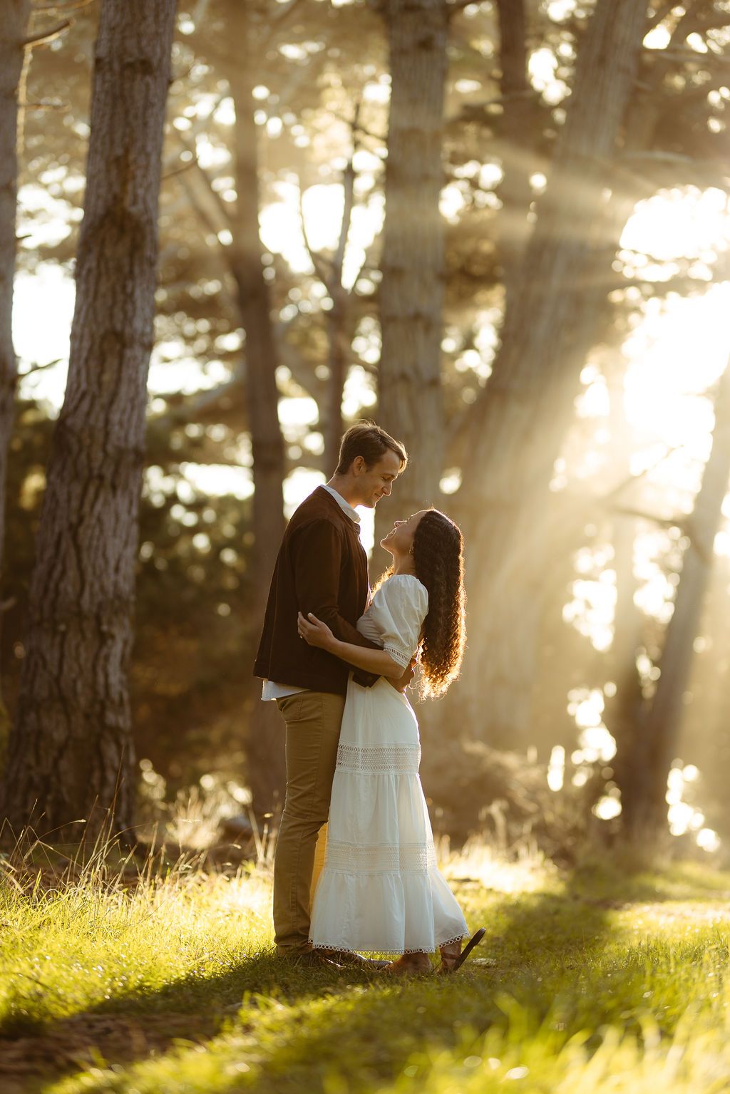 Couple embracing among sunlit pines as light streams through the trees, romantic forest elopement photography