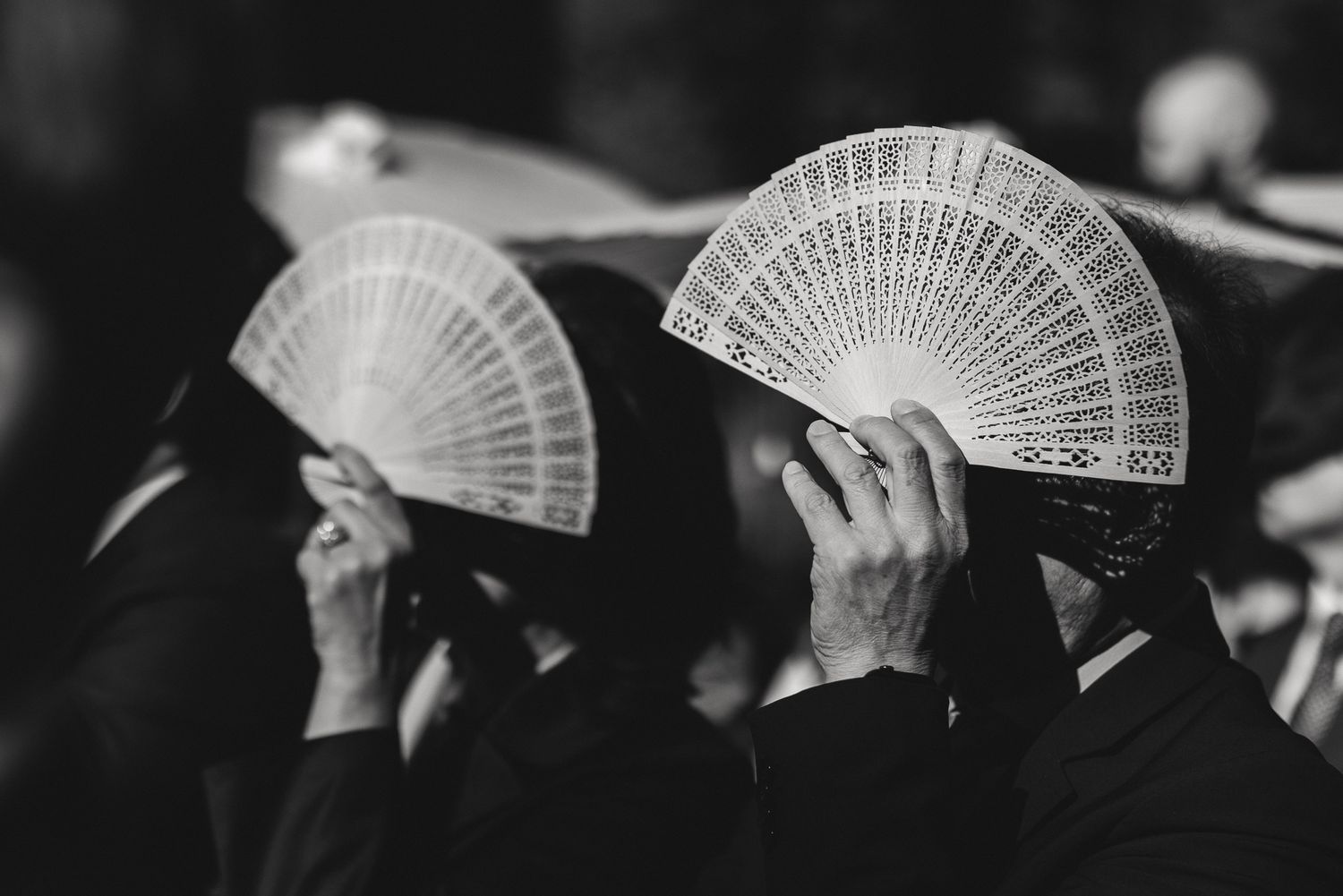 Cinematic black and white of the couple hidden behind decorative fans at a luxury wedding, by Sammy Aucella Photography