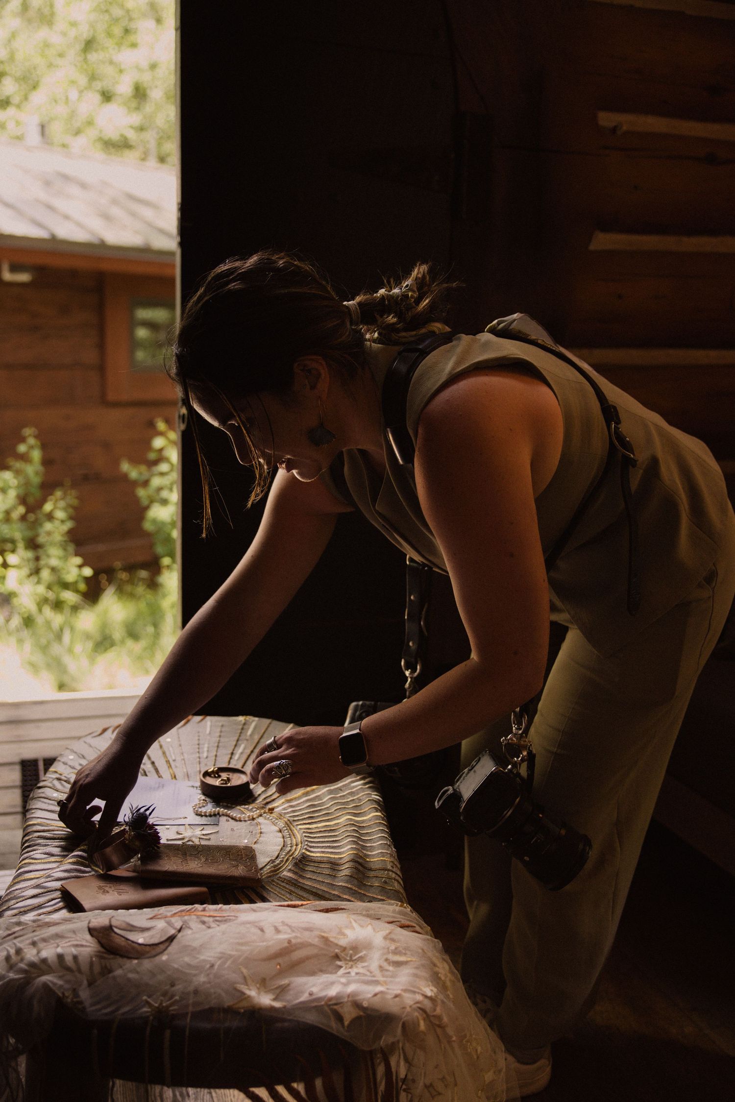 Woman in a green suit kneeling to style a table in a cabin doorway, behind the scenes of a lifestyle branding session