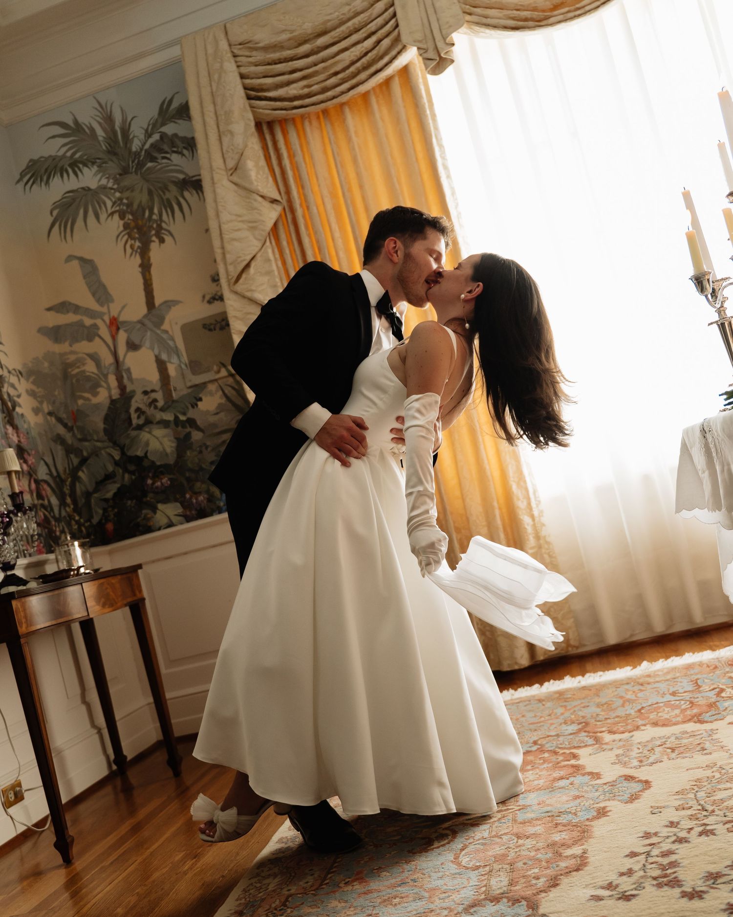 A romantic dip dance sequence between a couple in formal attire on an elegant carpeted floor with drapes in the background.
