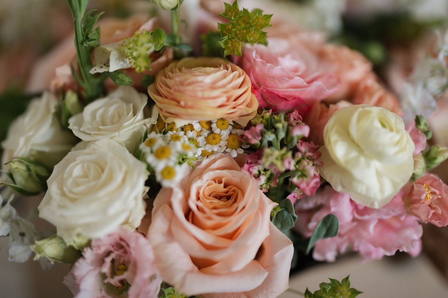Close-up of a romantic bridal bouquet with peach roses, white ranunculus, and pink blooms.