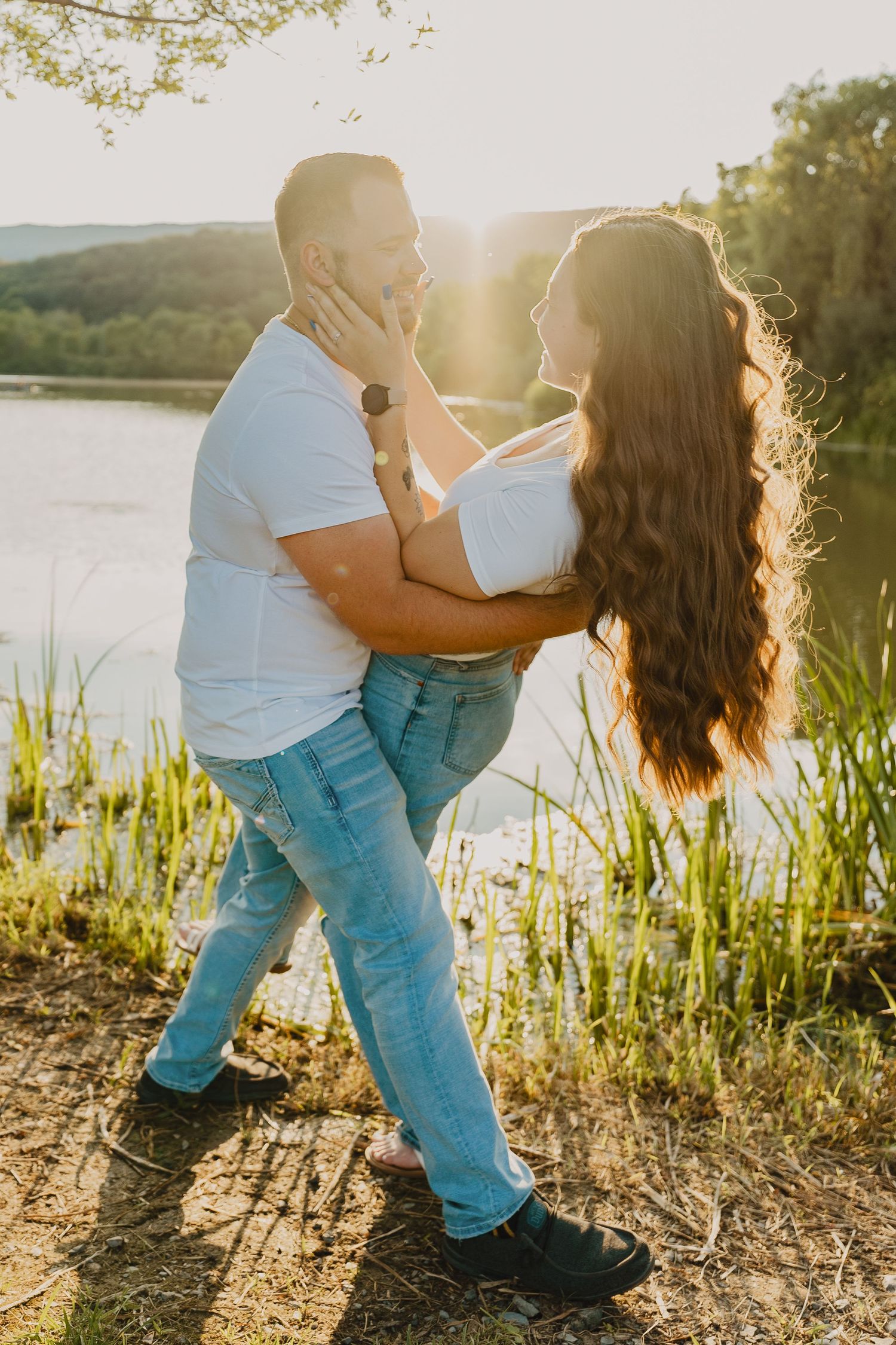 A tender moment between two people captured against a sun-lit lake backdrop.