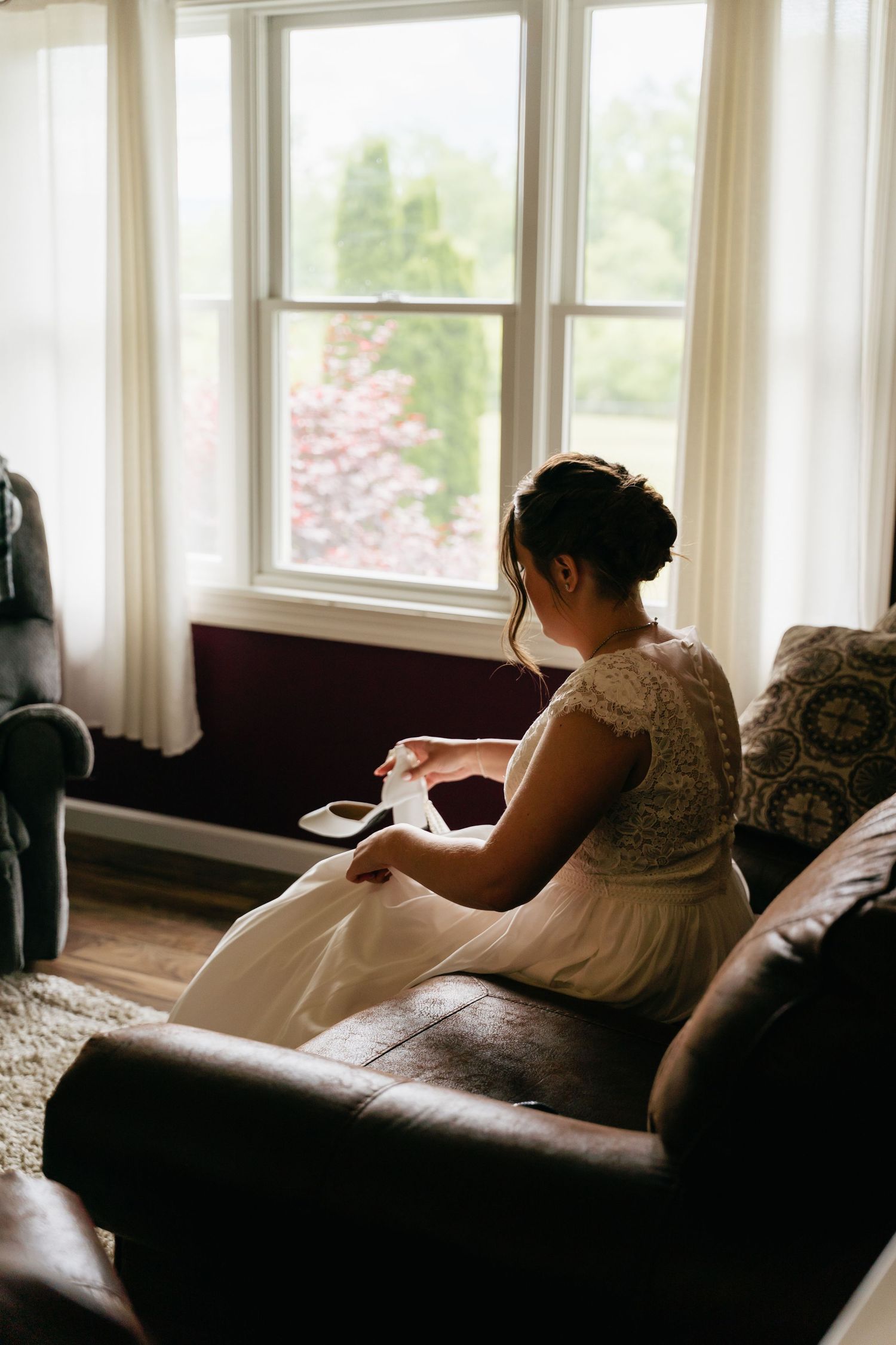 A person rests on a brown couch in a sunlit room with large windows.