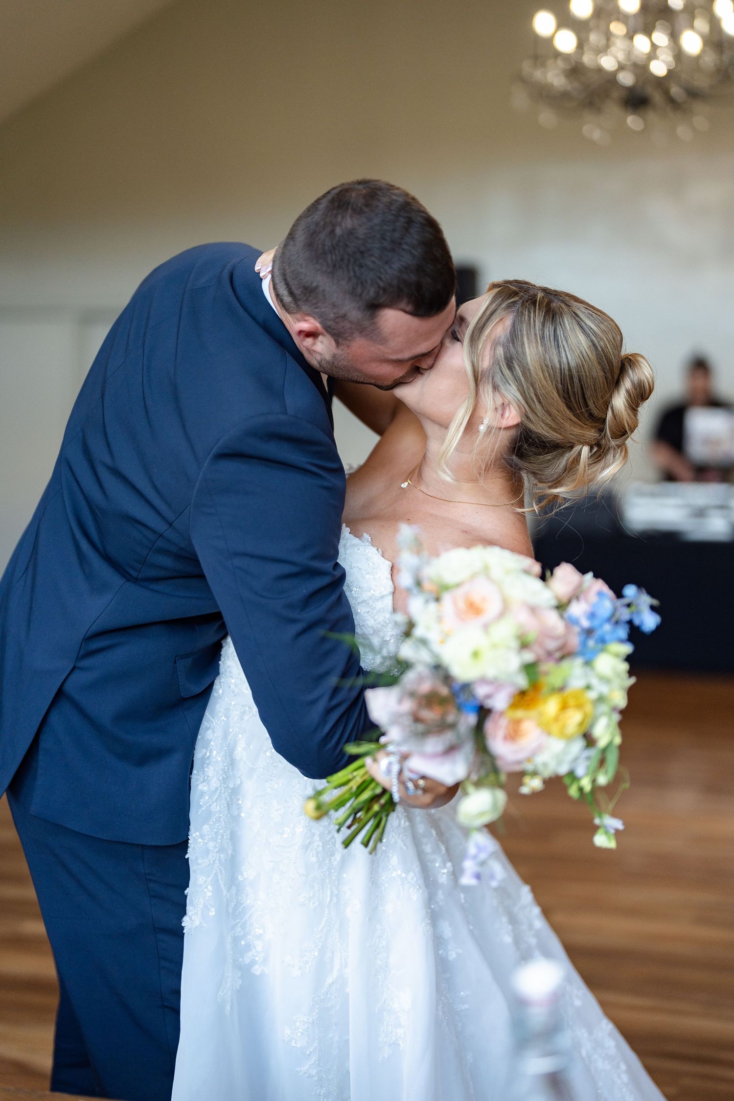 Bride and groom share a romantic kiss on the dance floor, bride holding a colorful pastel bouquet.