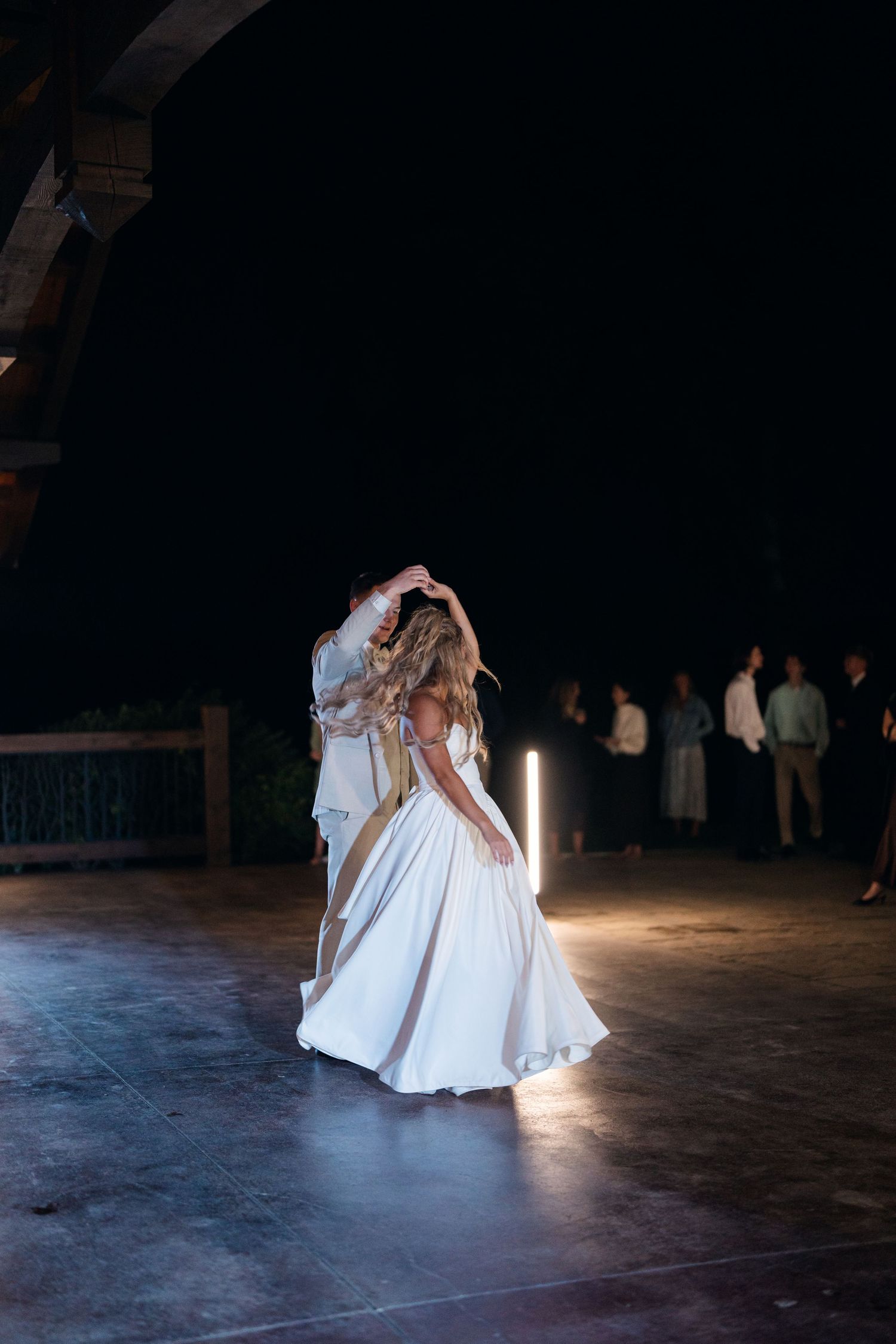 Bride and groom share their first dance in a dimly lit wedding venue with guests watching in the background.
