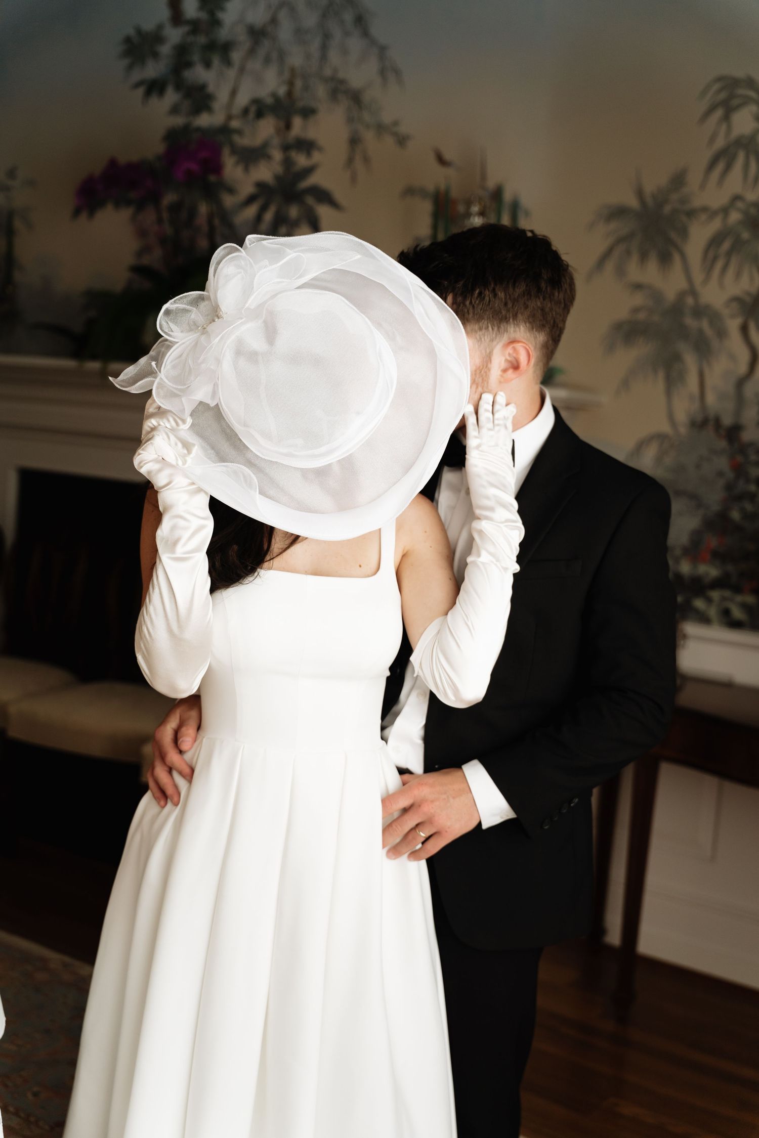 A romantic wedding couple shares an intimate dance moment in a room with palm tree wallpaper decor.