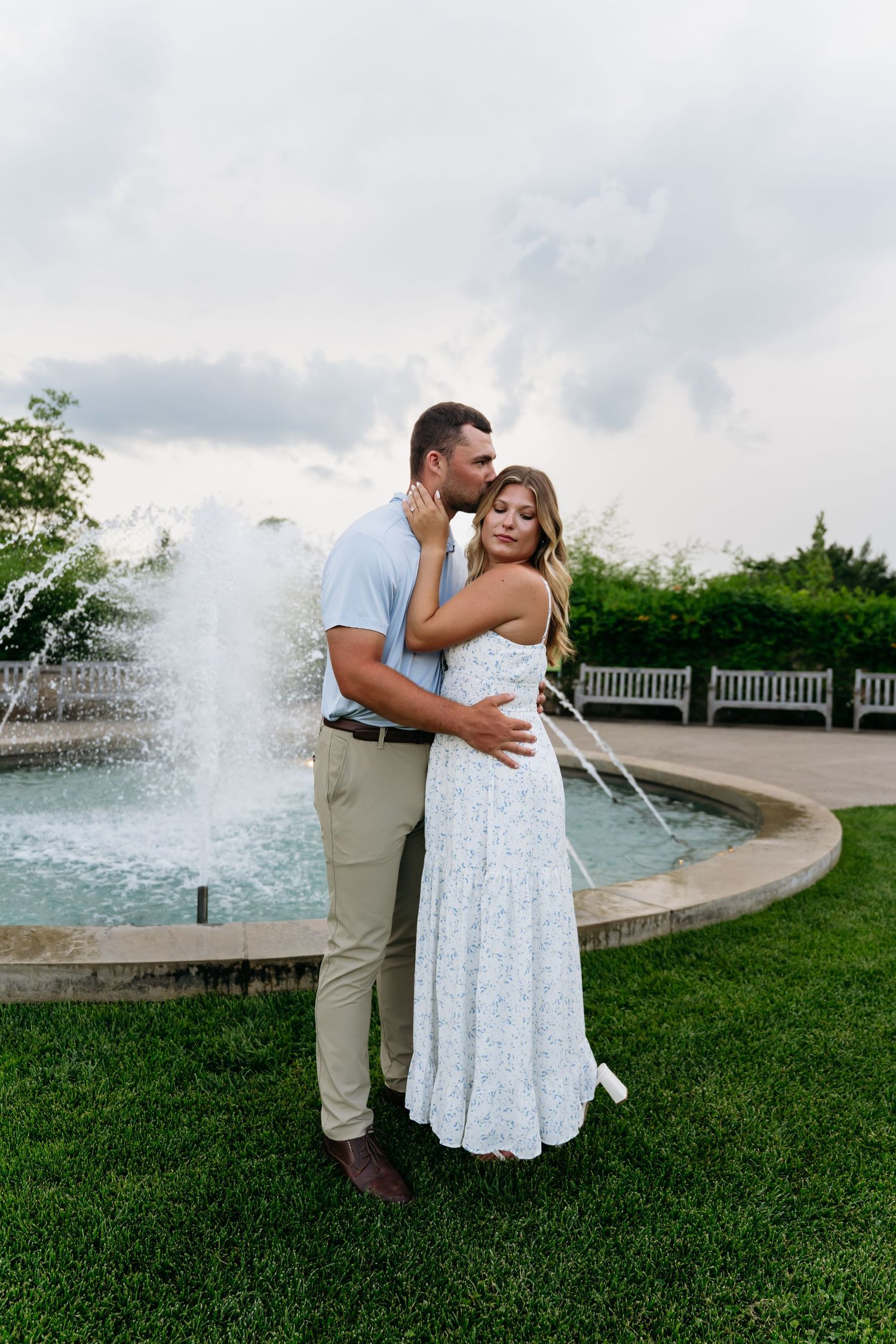 A couple embraces by a fountain in a garden setting, with the bride wearing a flowing white lace dress.