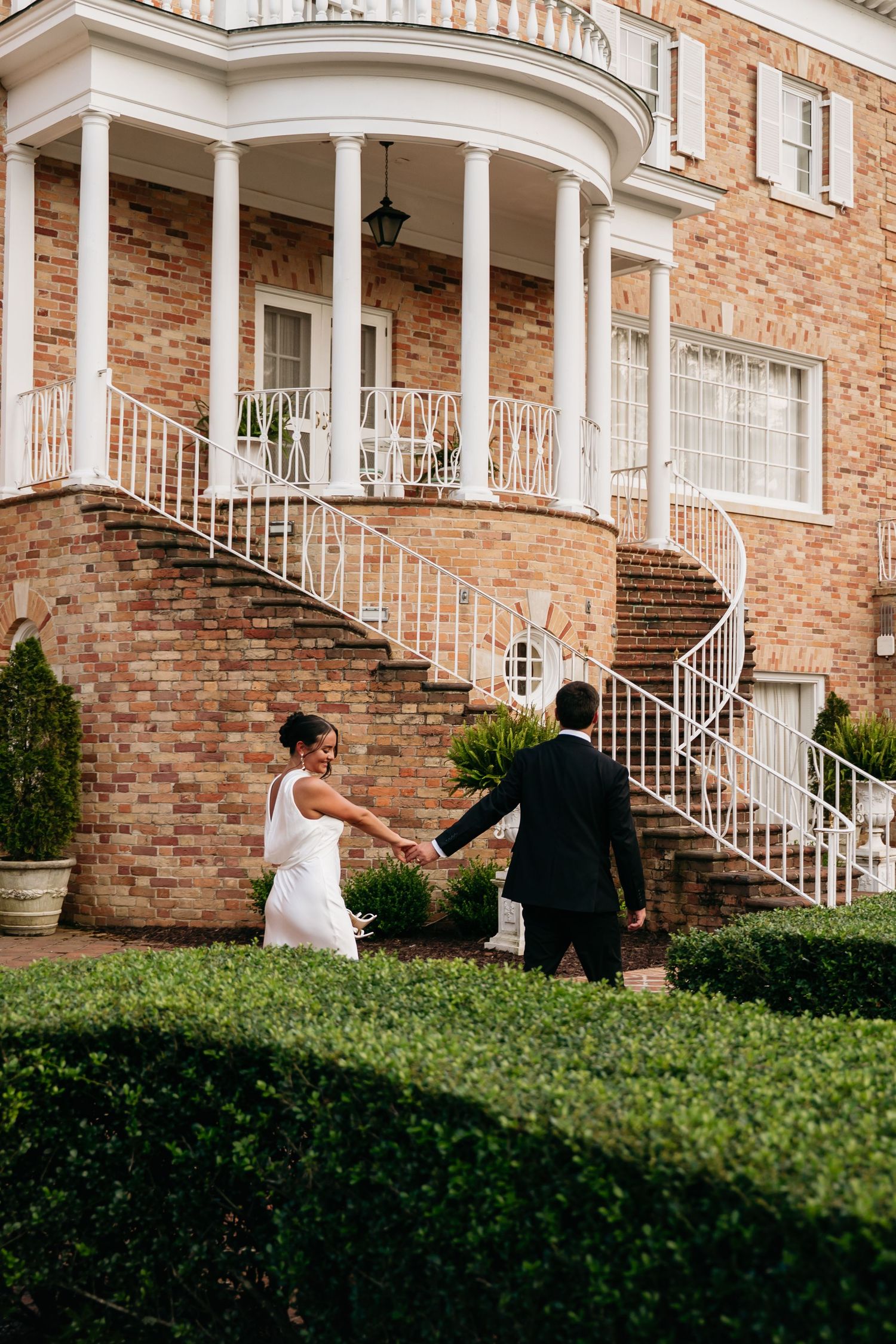 A couple poses together on the steps of a grand brick building with white columns and railings.