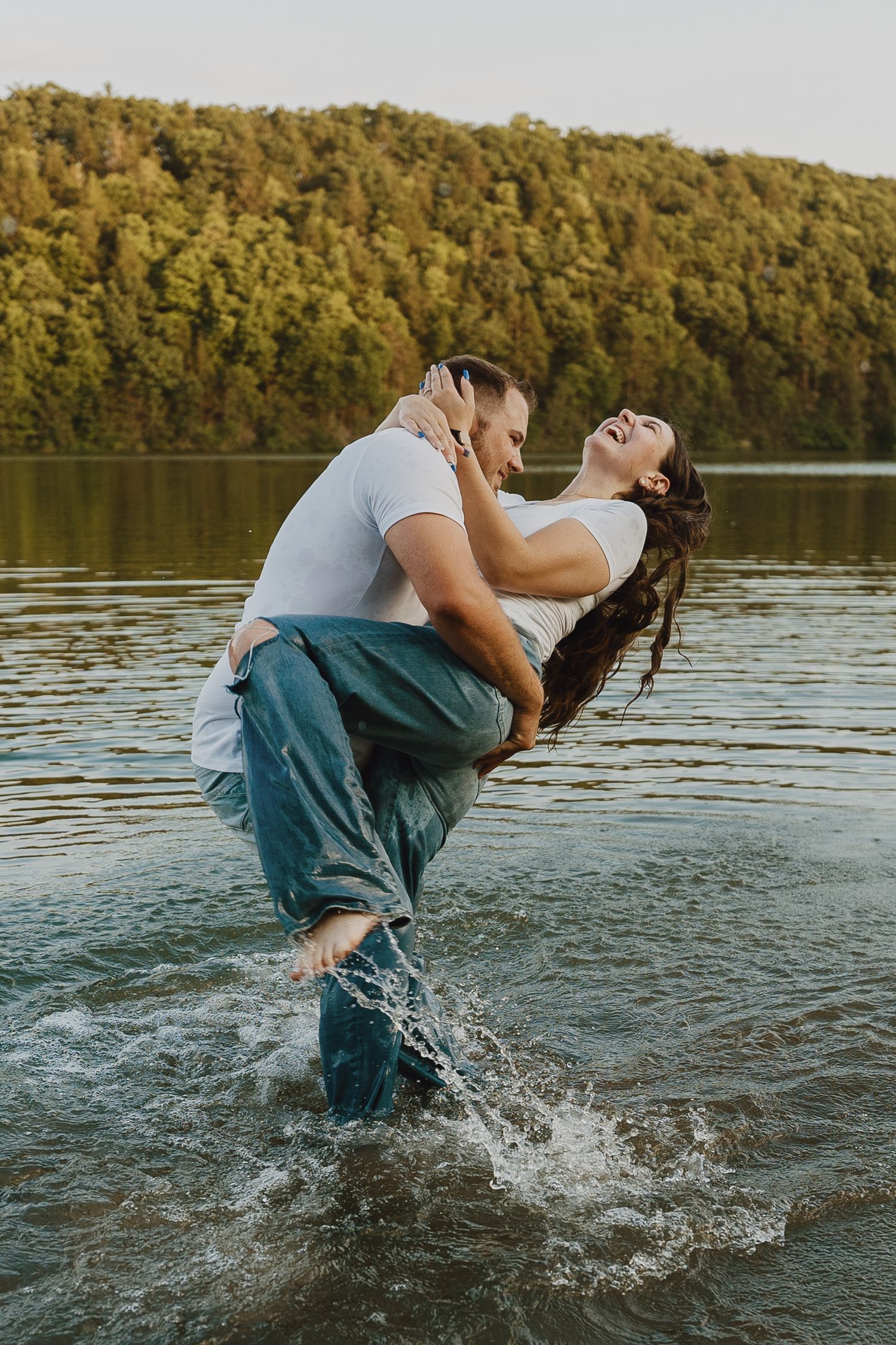 A romantic dip pose in the lake water with tree-covered hills in background.