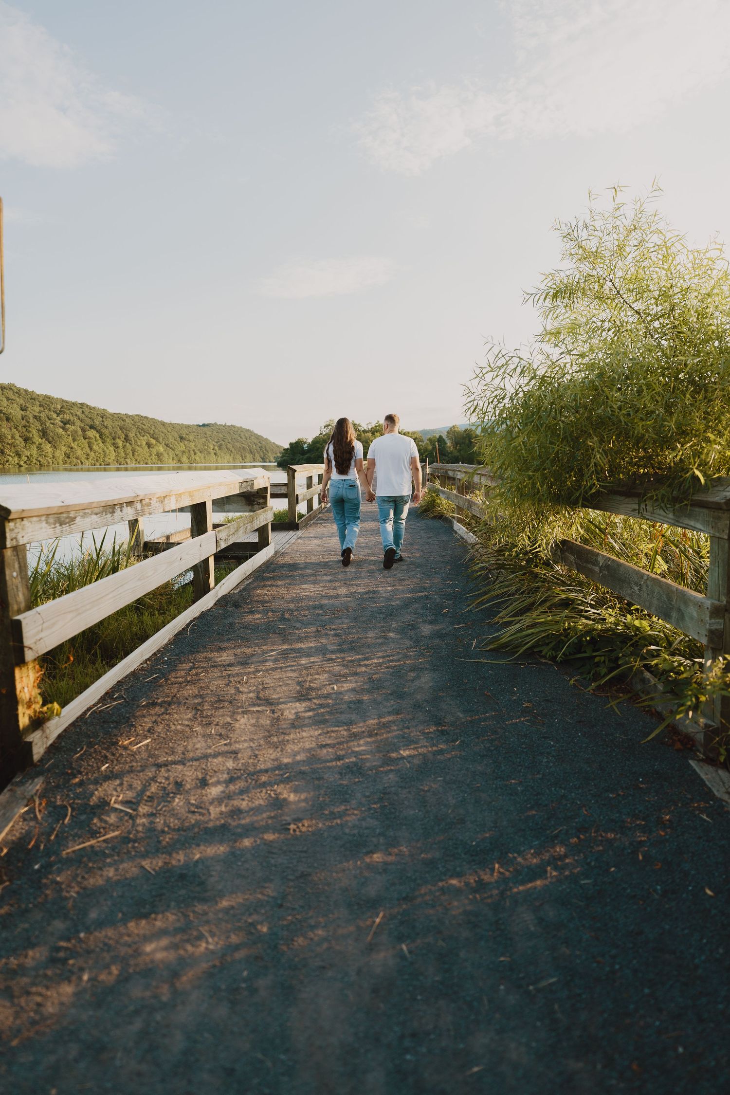 A couple walks away on a wooden boardwalk surrounded by nature and water.