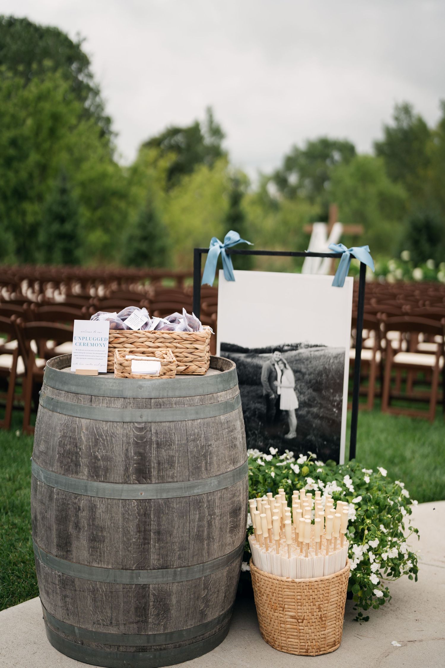 Rustic wine barrel wedding ceremony decor with wicker basket, sparklers, and black and white photo display outdoors.