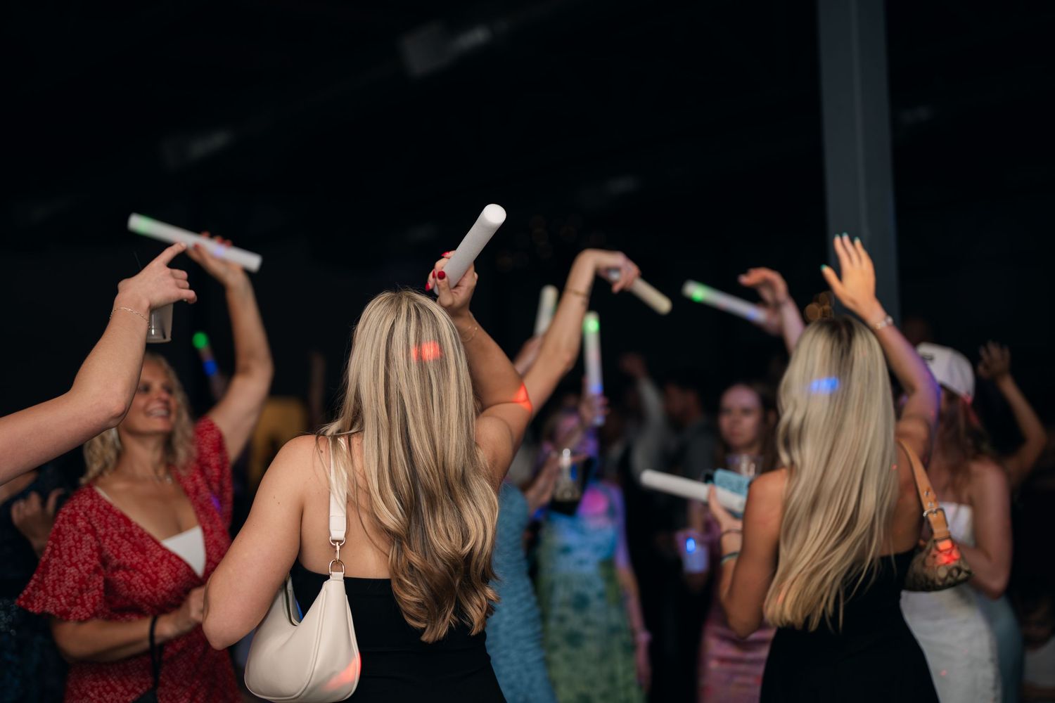 Wedding reception guests dancing with glowing light sticks in a darkened celebration venue.