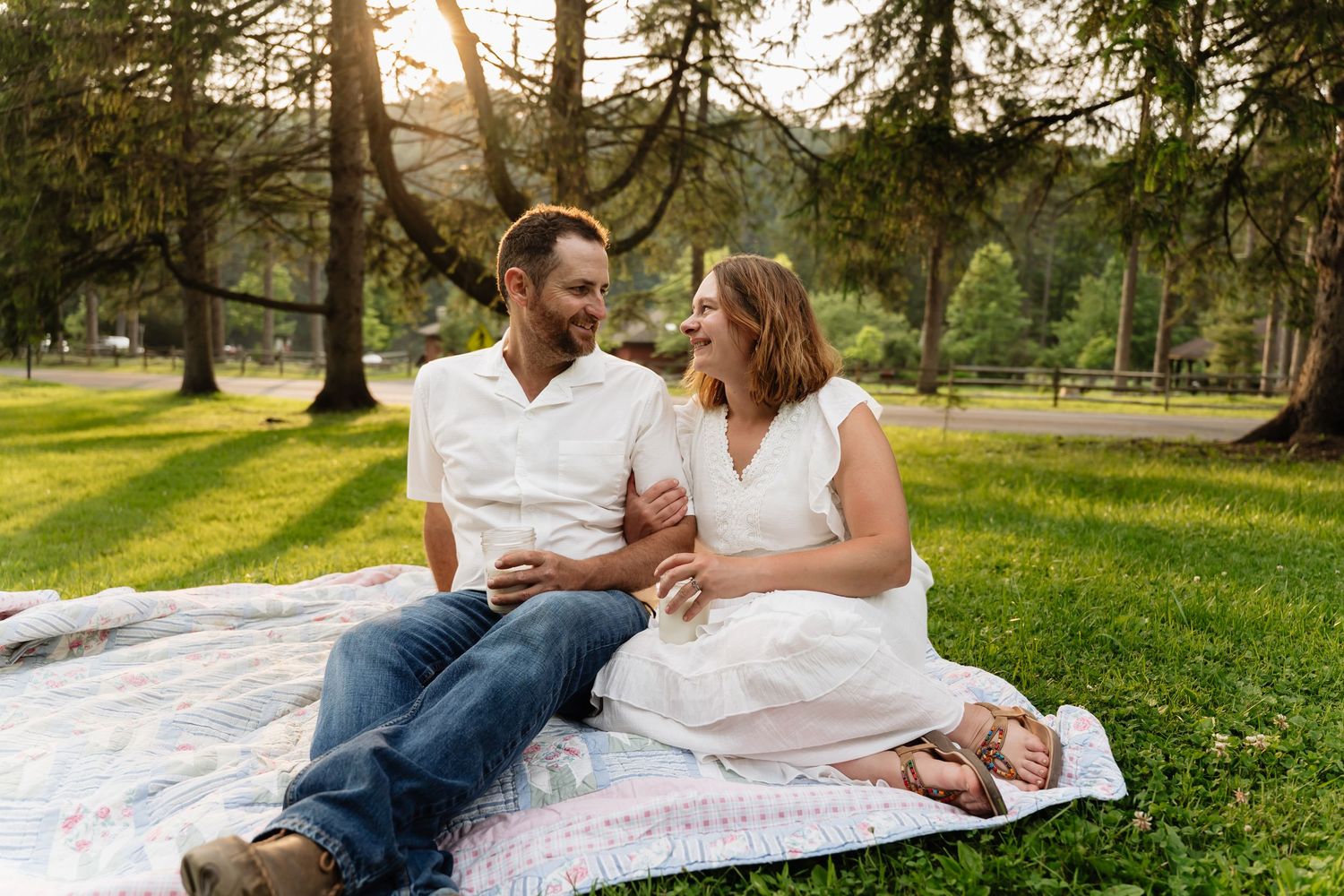 A couple lies on a white blanket in a sunny park setting having a sweet moment together during a summer afternoon.