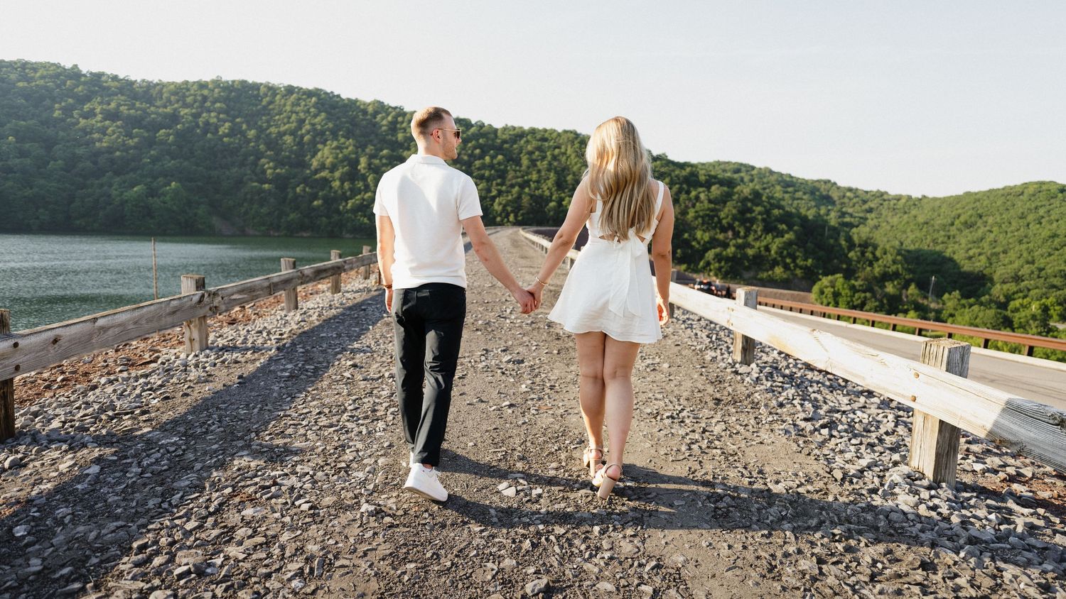 Couple walking along scenic mountain overlook path during sunset.