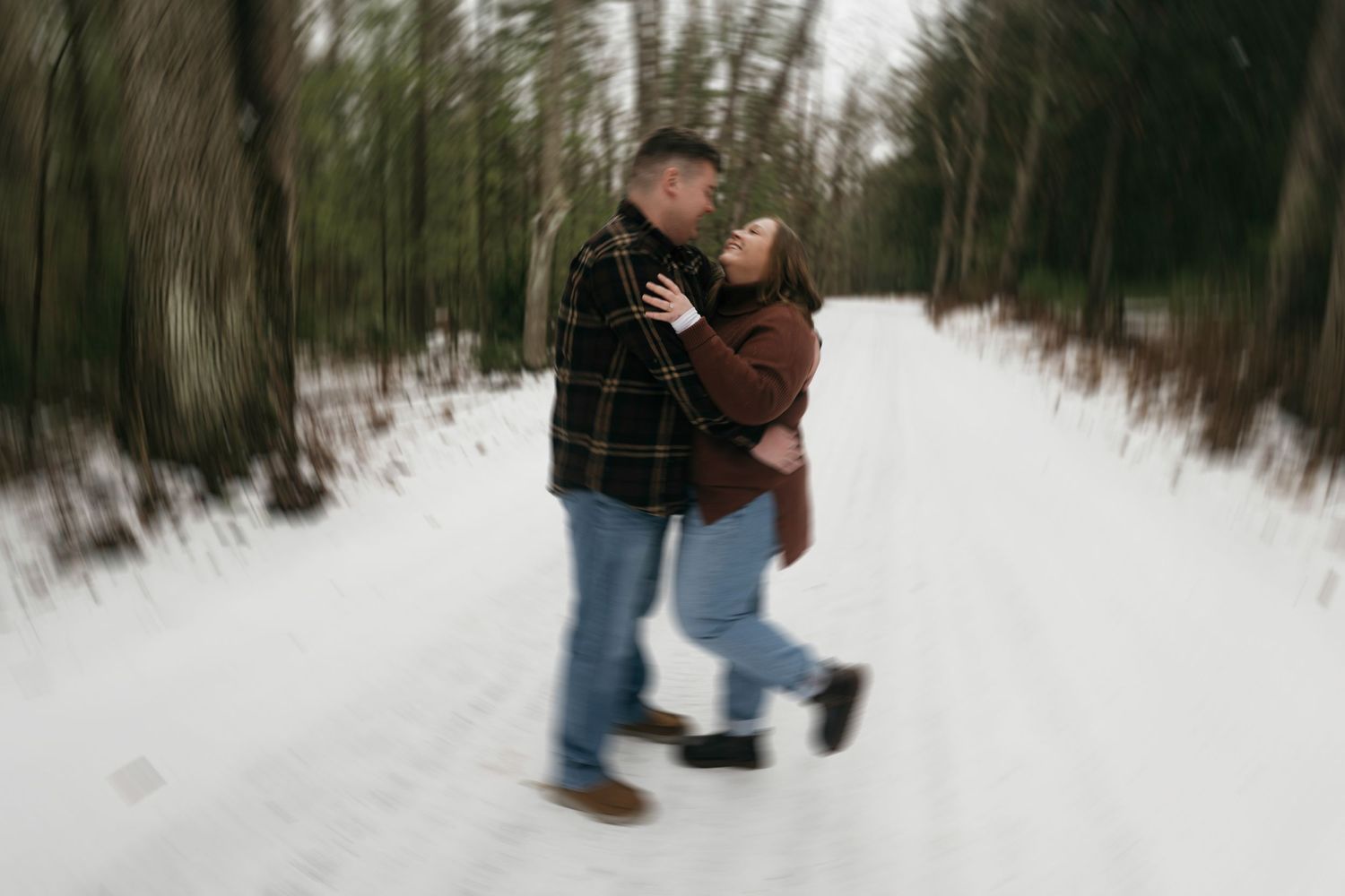 A romantic winter scene shows a couple embracing on a snow-covered path through the woods.