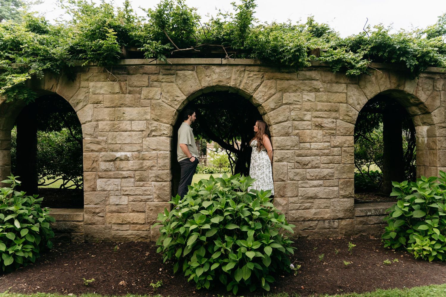 A stone archway with green foliage creates a scenic entrance along a garden path.